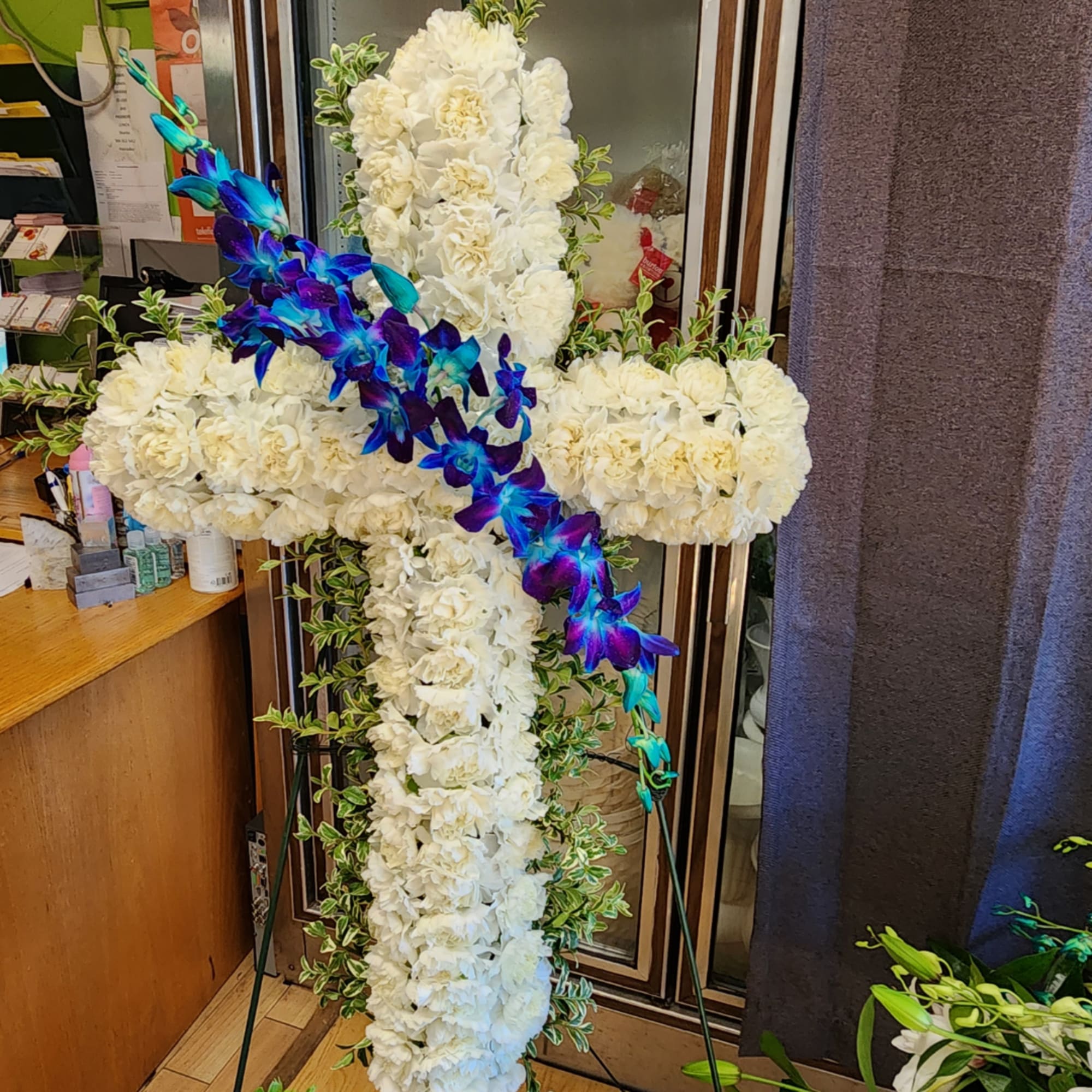 White floral cross on a stand with a blue-purple orchid garland