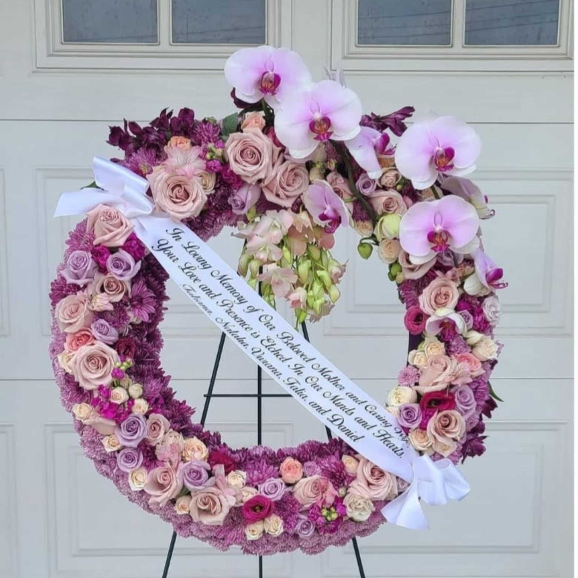 Heart-shaped floral wreath with pink roses and orchids on an easel