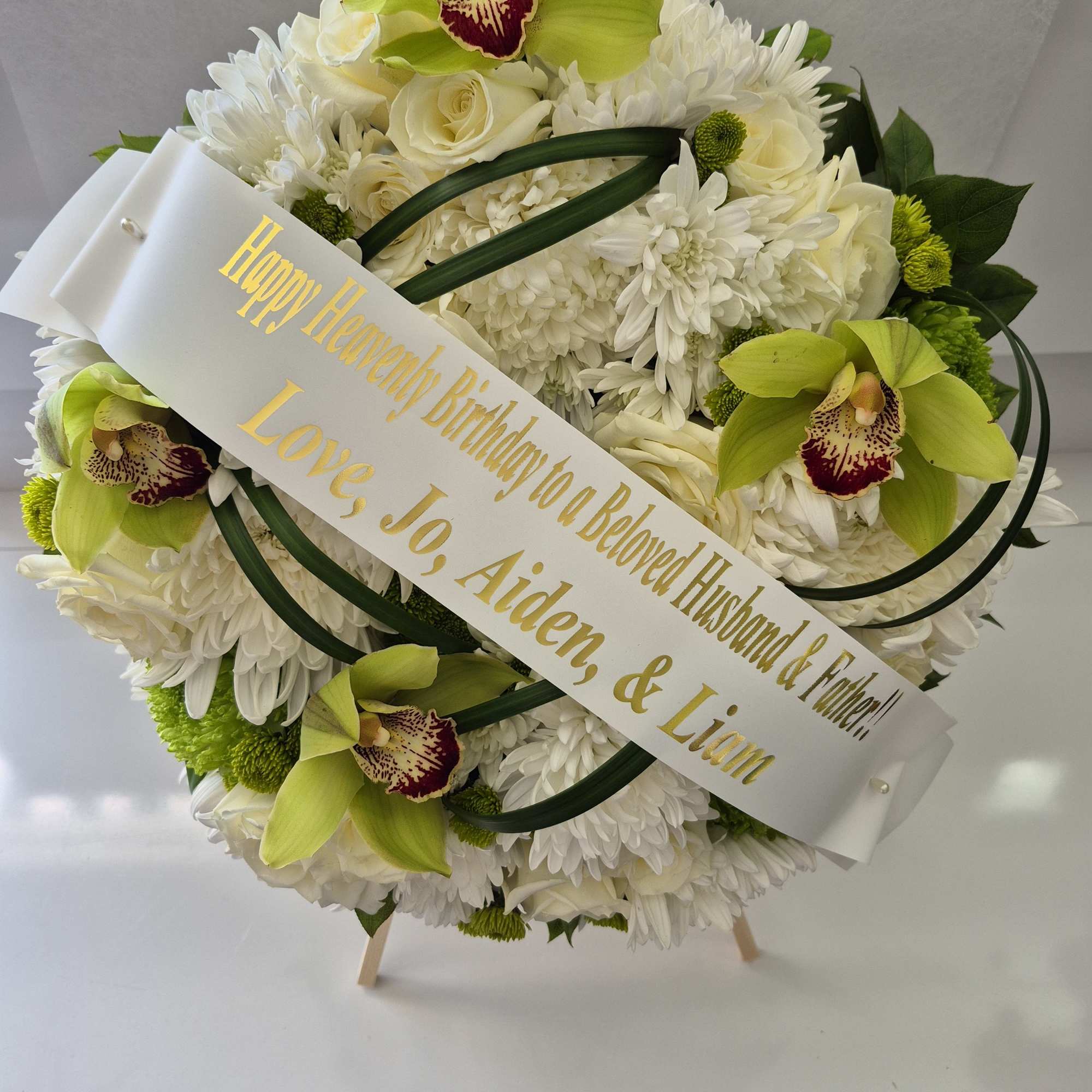 White floral wreath with green orchids and a birthday ribbon