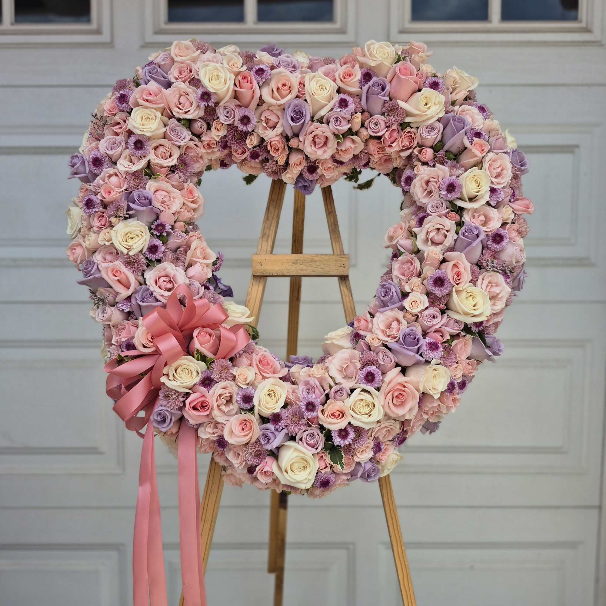 Heart-shaped floral wreath of pink, lavender, and cream roses on an easel