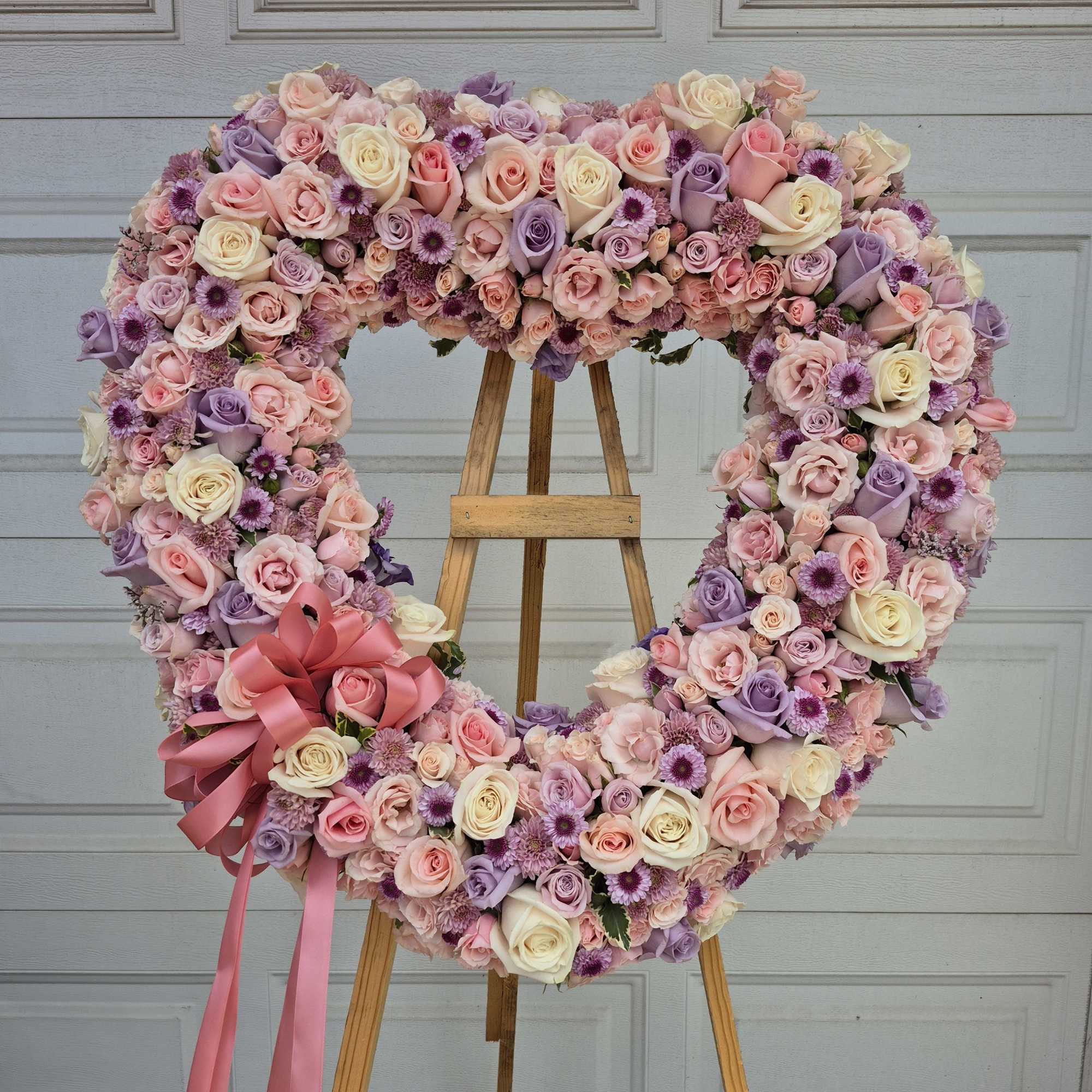 Heart-shaped floral wreath of pink, lavender, and cream roses on an easel