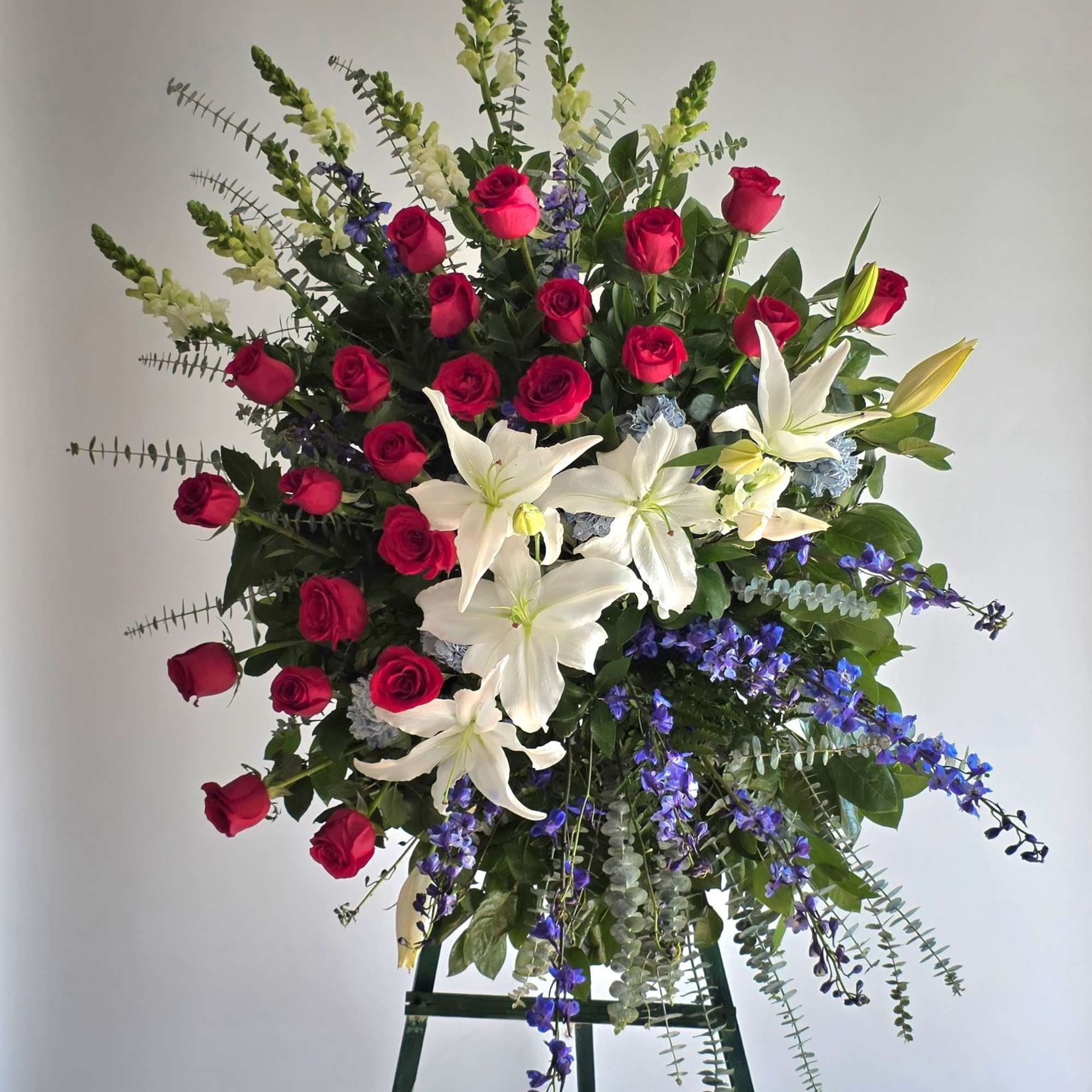 Standing floral spray with red roses, white lilies, and blue flowers