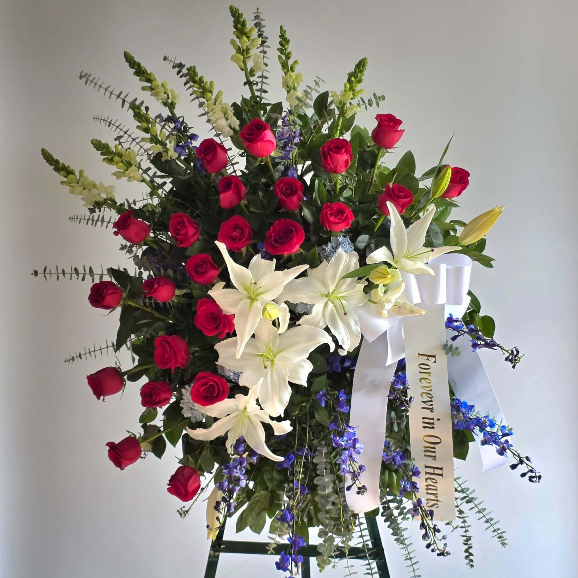 Standing floral spray with red roses, white lilies, and a white ribbon