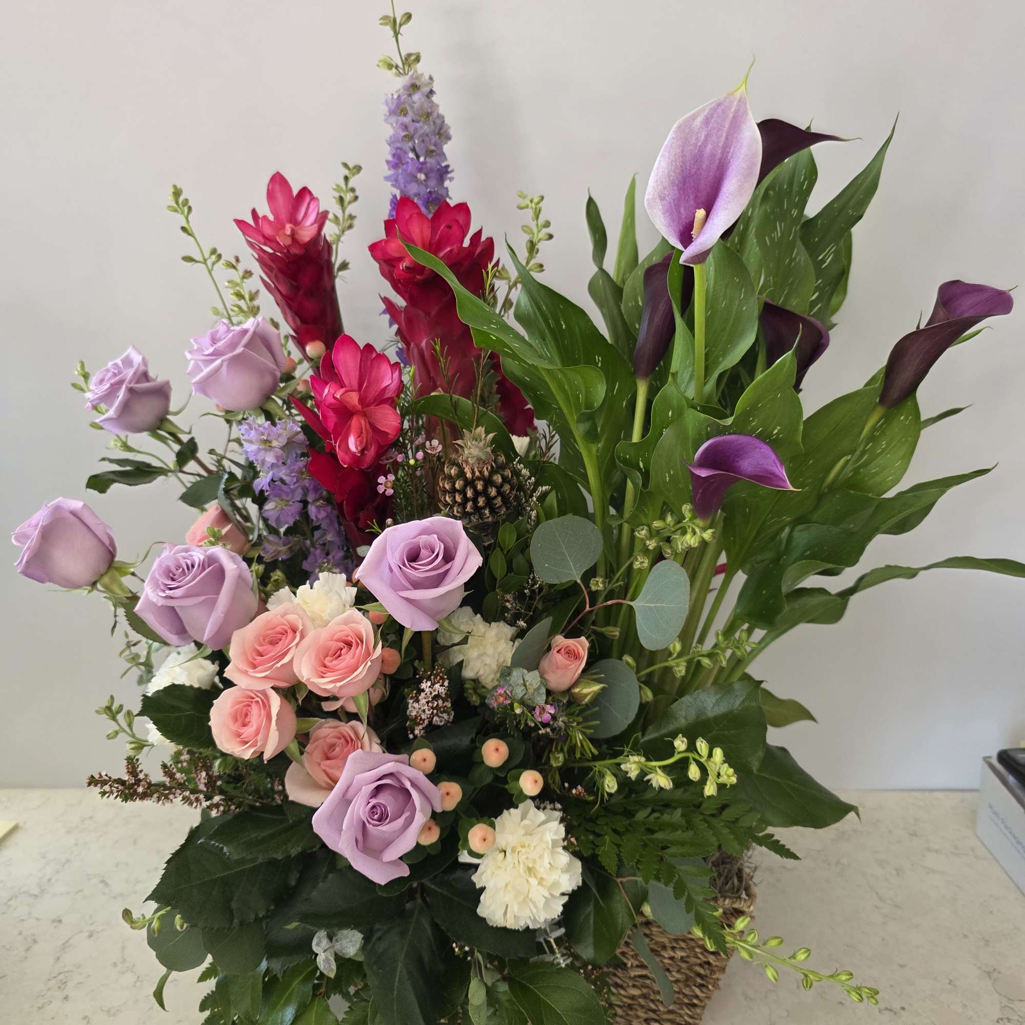 Mixed bouquet with lavender roses, purple calla lilies, and pink blooms in a basket