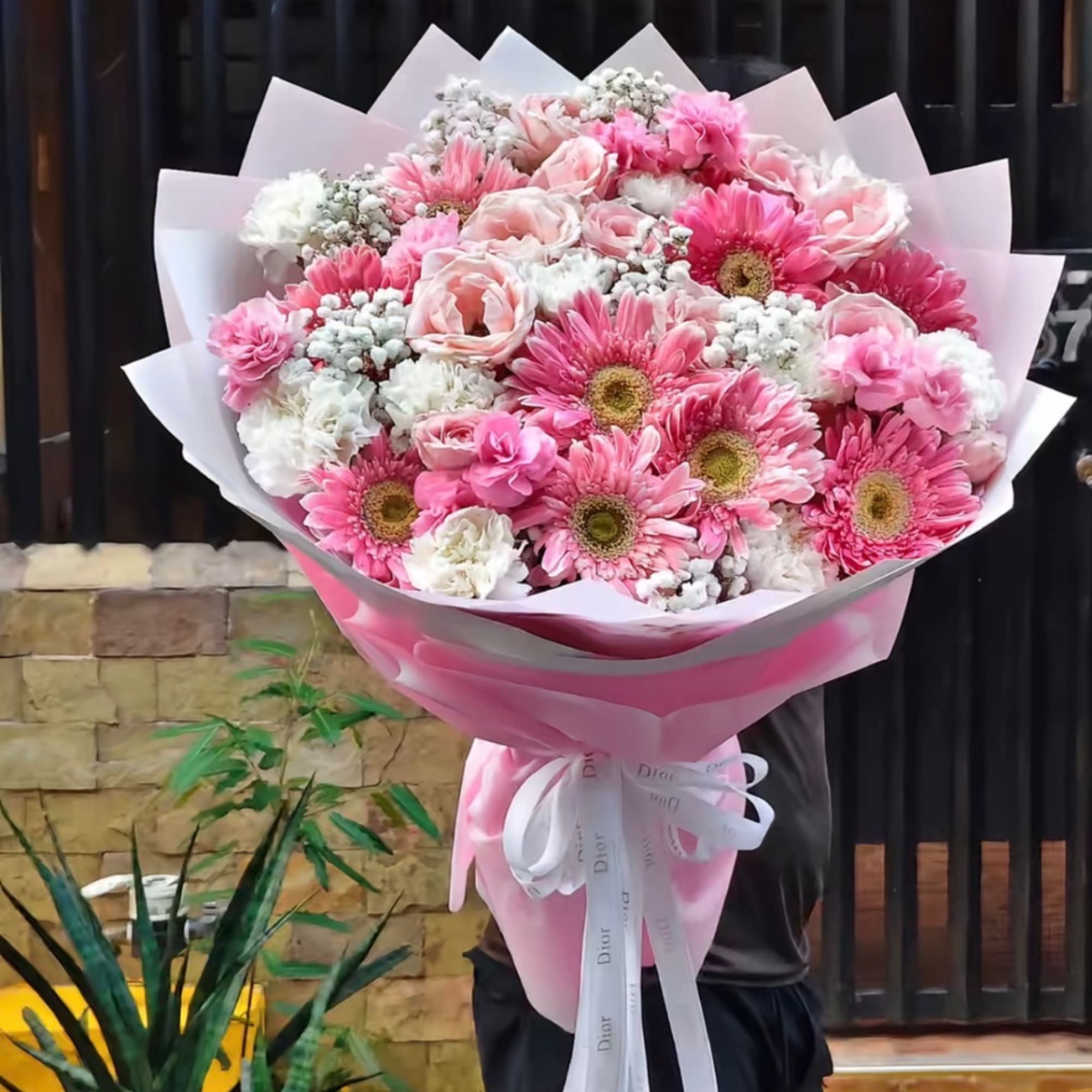 Large bouquet of pink gerbera daisies, roses, and white carnations wrapped in pink paper