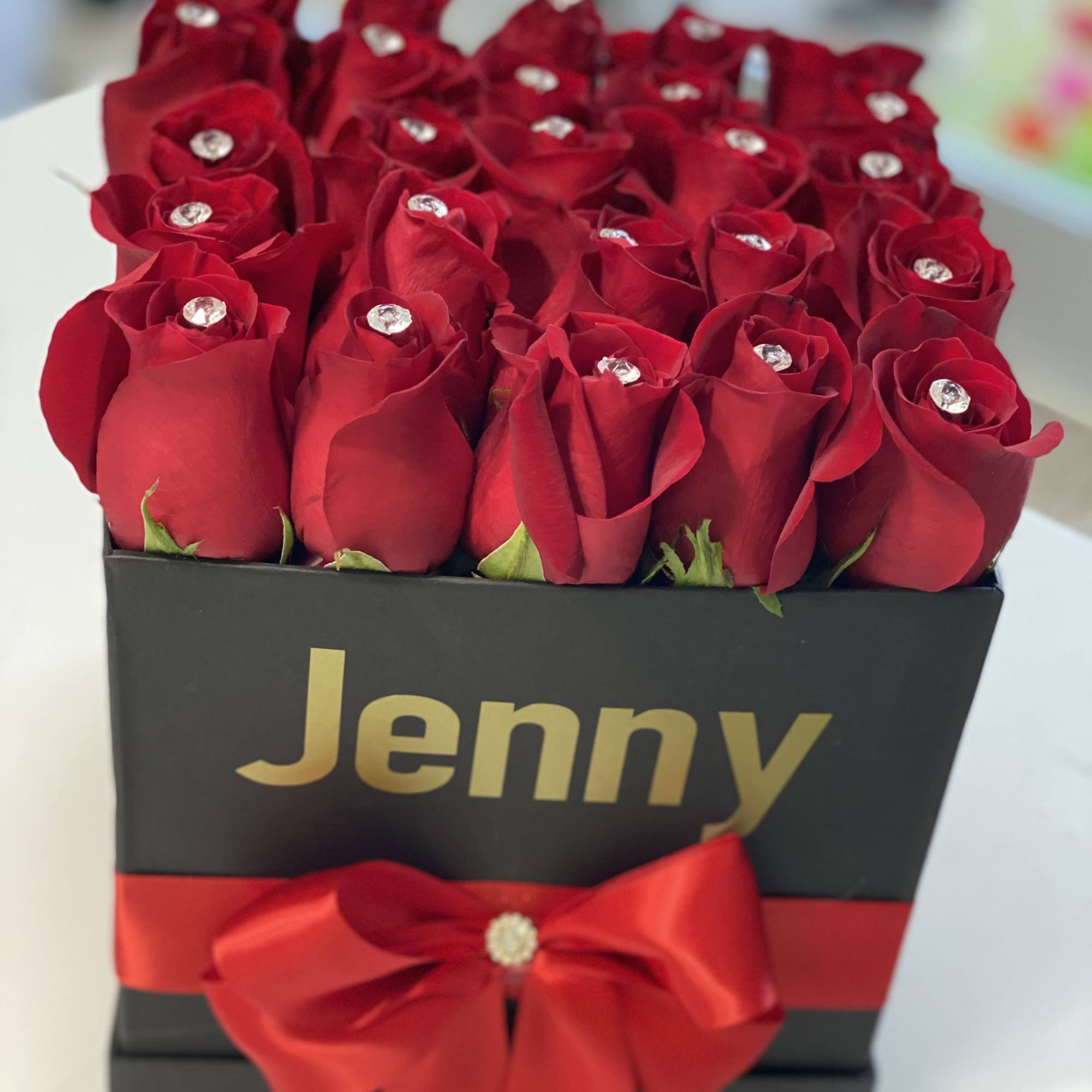 Red roses in a black gift box with a red ribbon and gold lettering