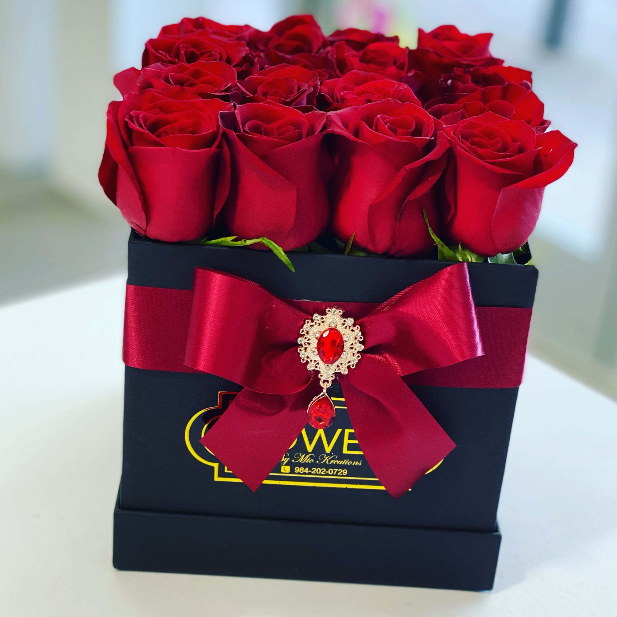 Red roses arranged in a black gift box with a red ribbon bow