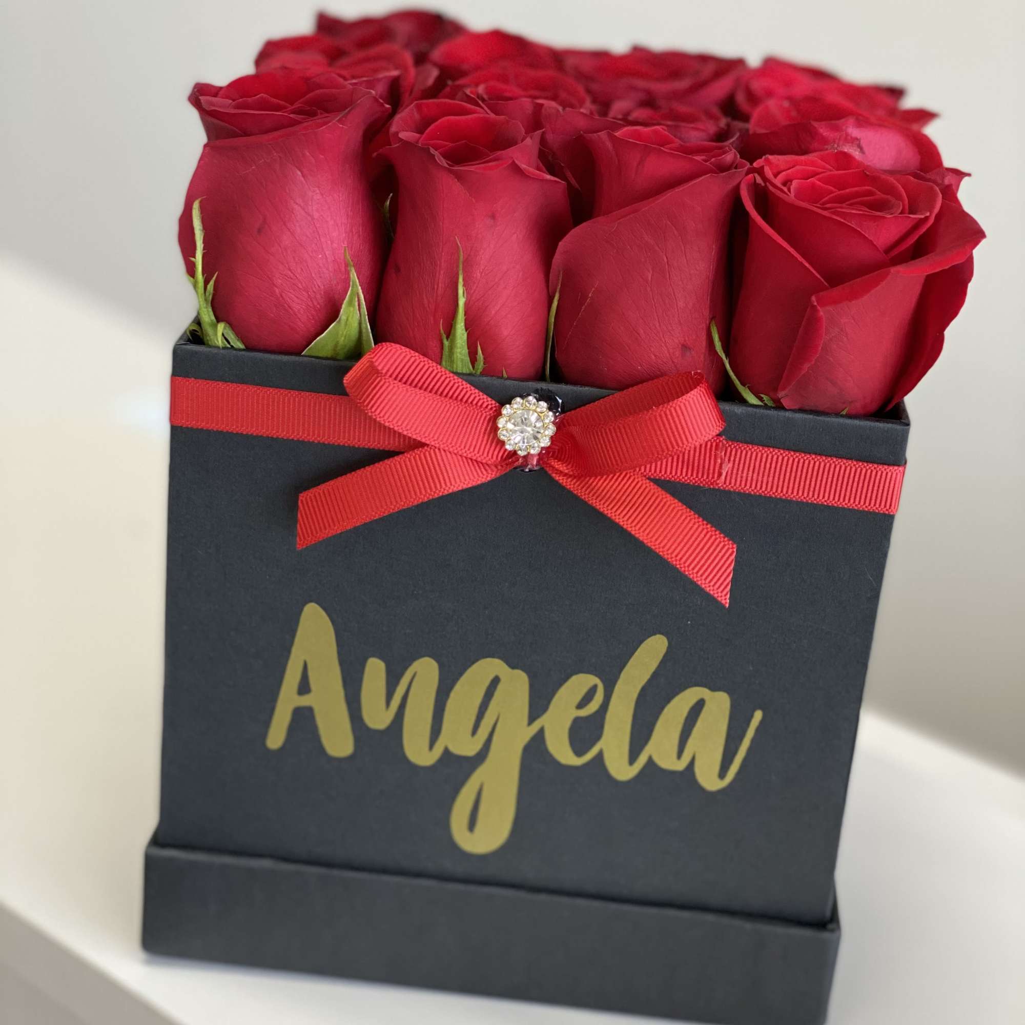 Red roses arranged in a black gift box with a red ribbon