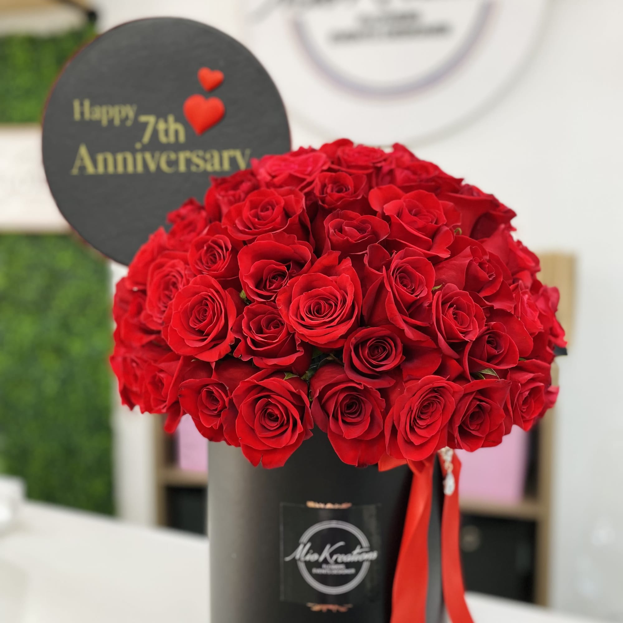 Red roses arranged in a black hatbox with a "Happy 7th Anniversary" sign