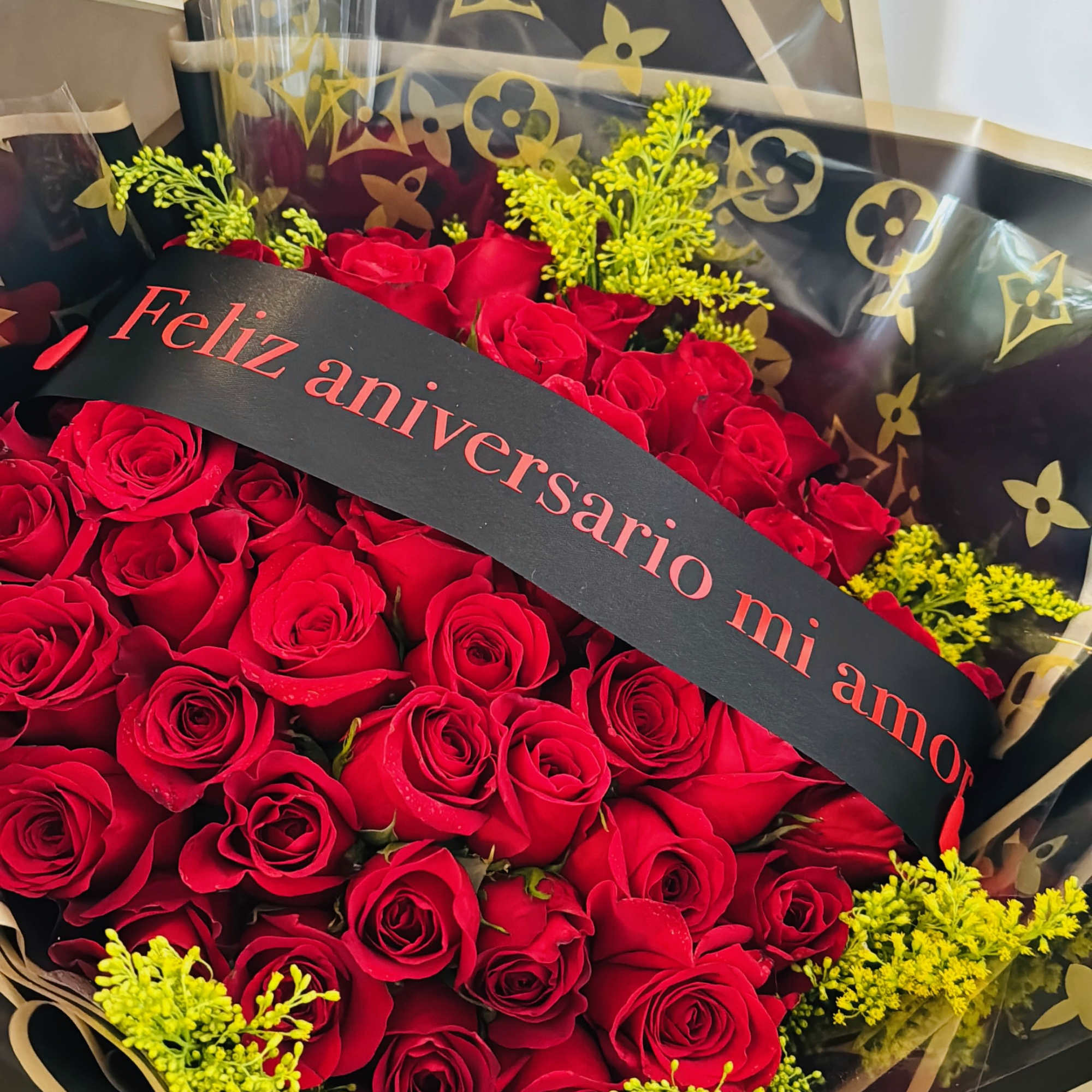 Bouquet of red roses with yellow filler and a "Feliz aniversario mi amor" ribbon