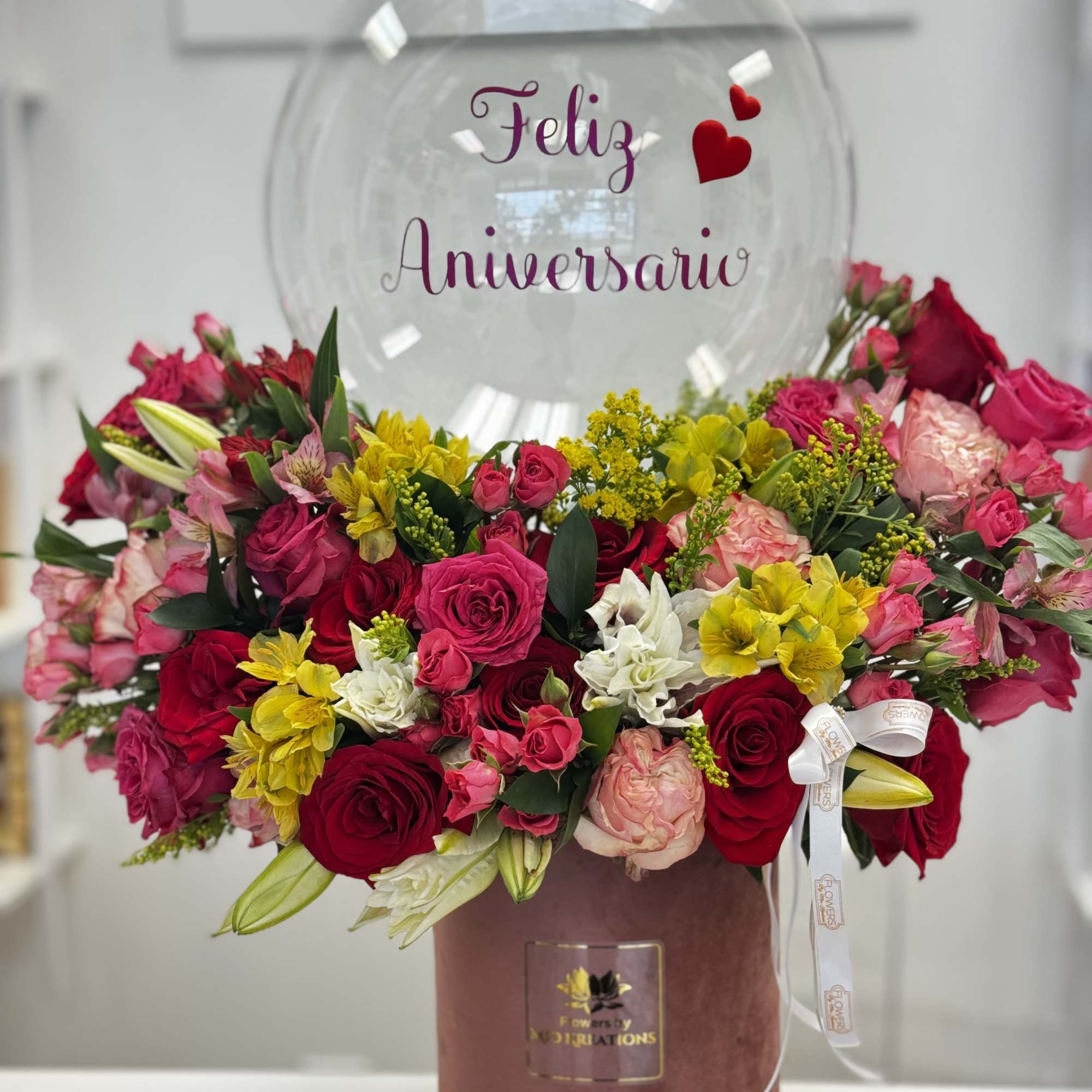 Mixed pink, red, yellow, and white flowers in a pink box with a clear anniversary balloon.