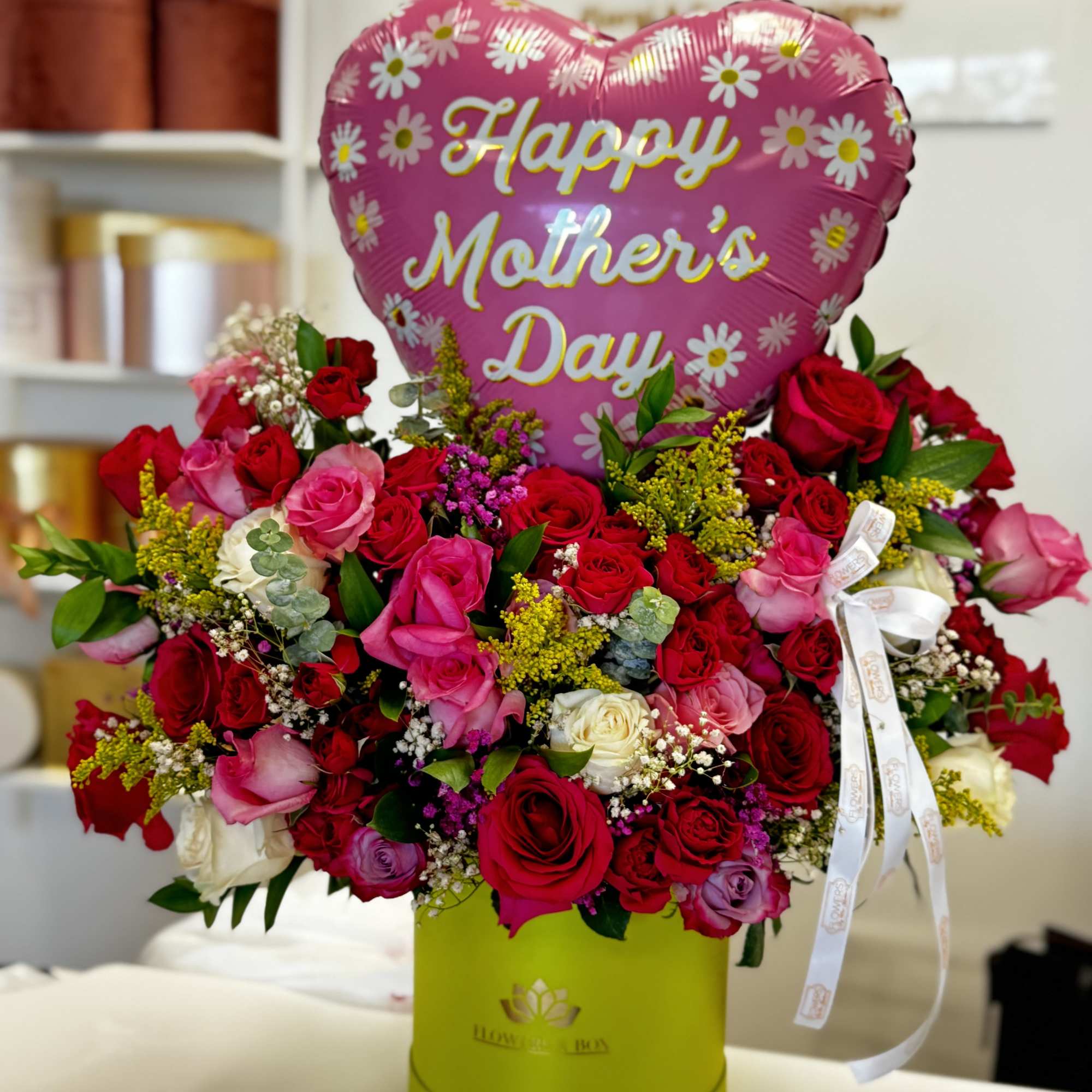 Pink heart balloon above a mixed rose arrangement in a green box