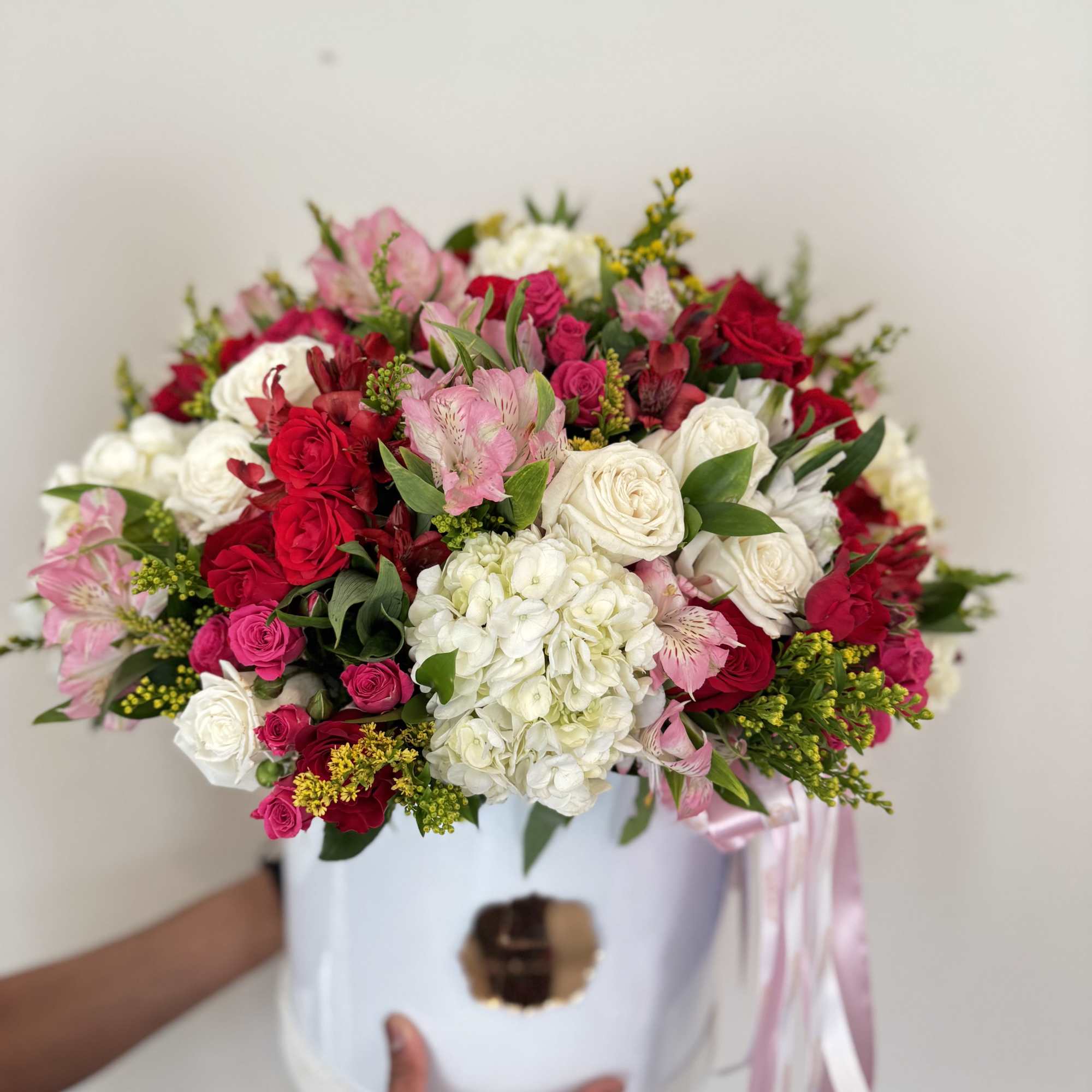 Mixed pink, red, and white flower arrangement in a white hat box with ribbon