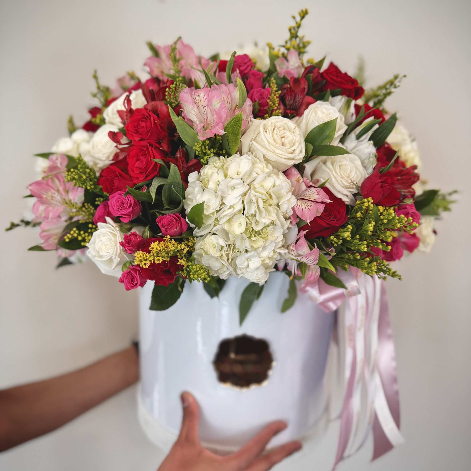 Large bouquet of red, pink, and white flowers in a white hat box with ribbon