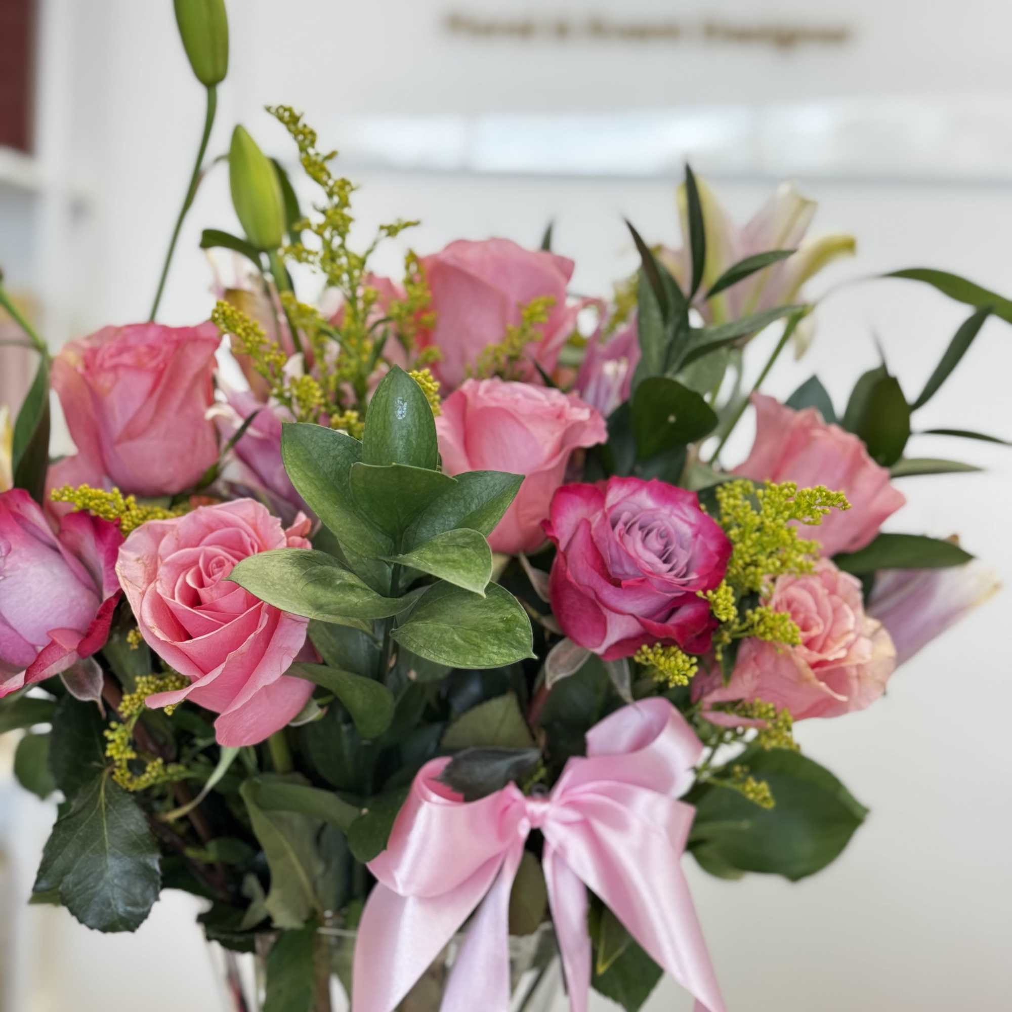 Pink roses and lilies in a clear vase with a pink ribbon