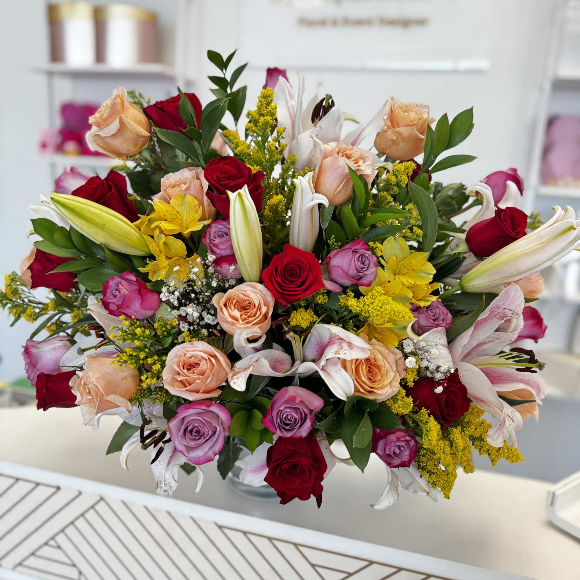 Mixed bouquet of roses, lilies, and yellow filler flowers in a vase