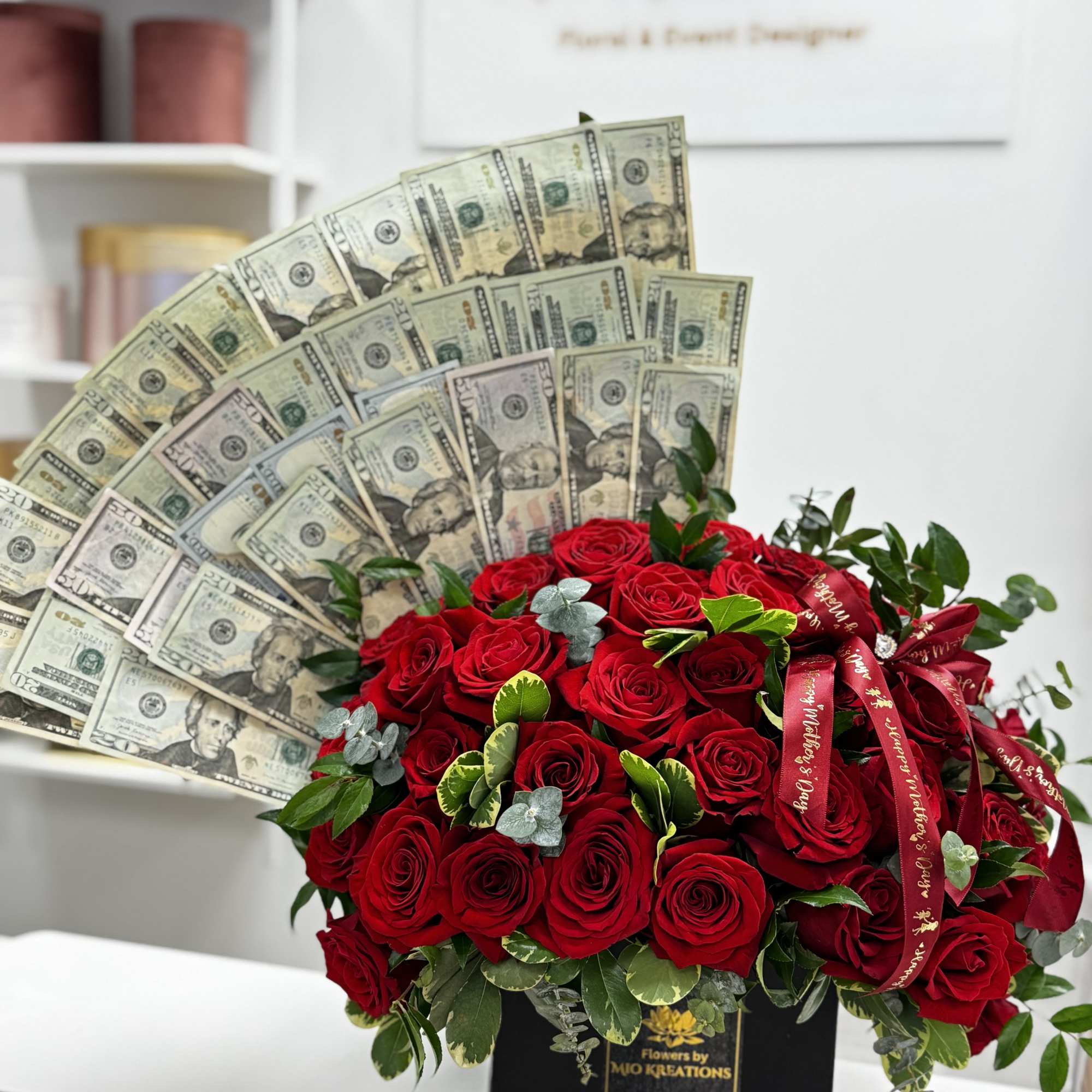 Red rose arrangement with fan-shaped dollar bills and ribbon in a black box