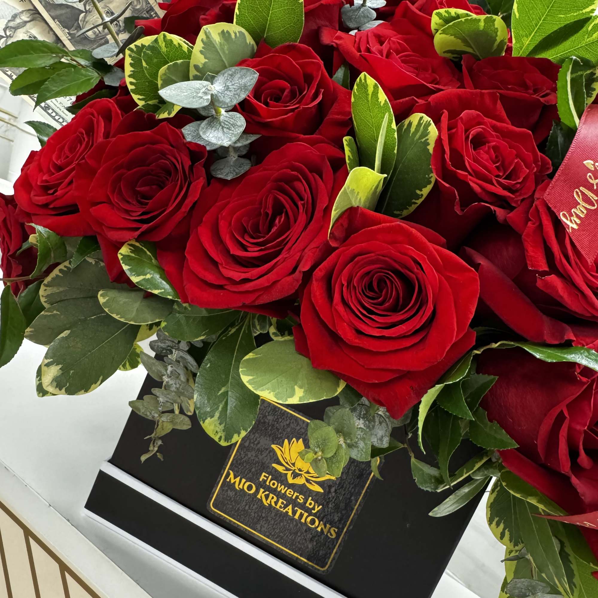 Red roses arranged in a black gift box with mixed greenery