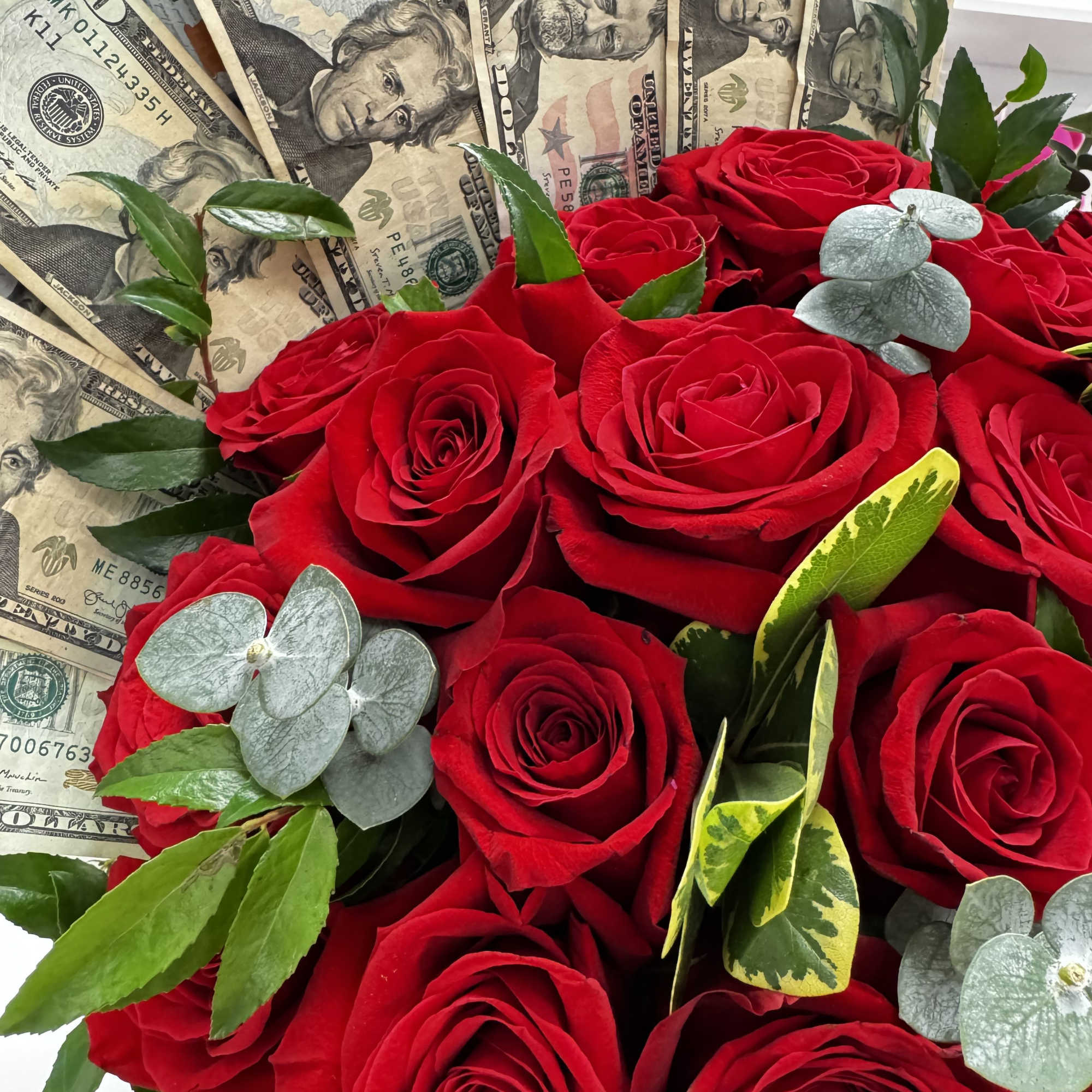 Bouquet of red roses with dollar bills and greenery accents