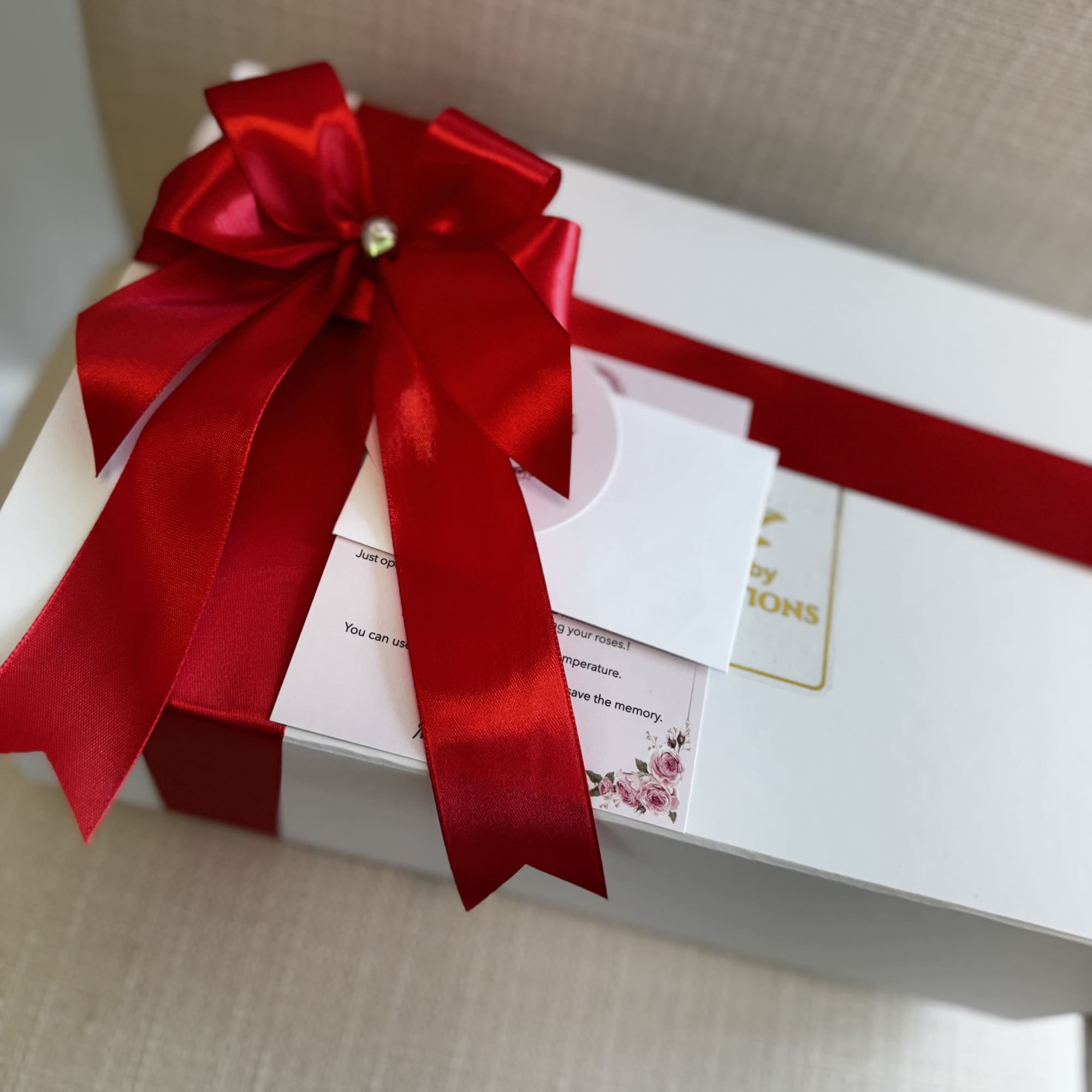 White gift box with a large red satin bow and cards on top