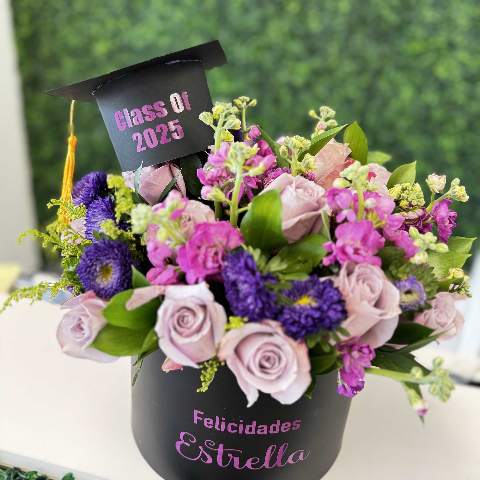 Pink and purple flower arrangement in a black graduation box with a cap topper