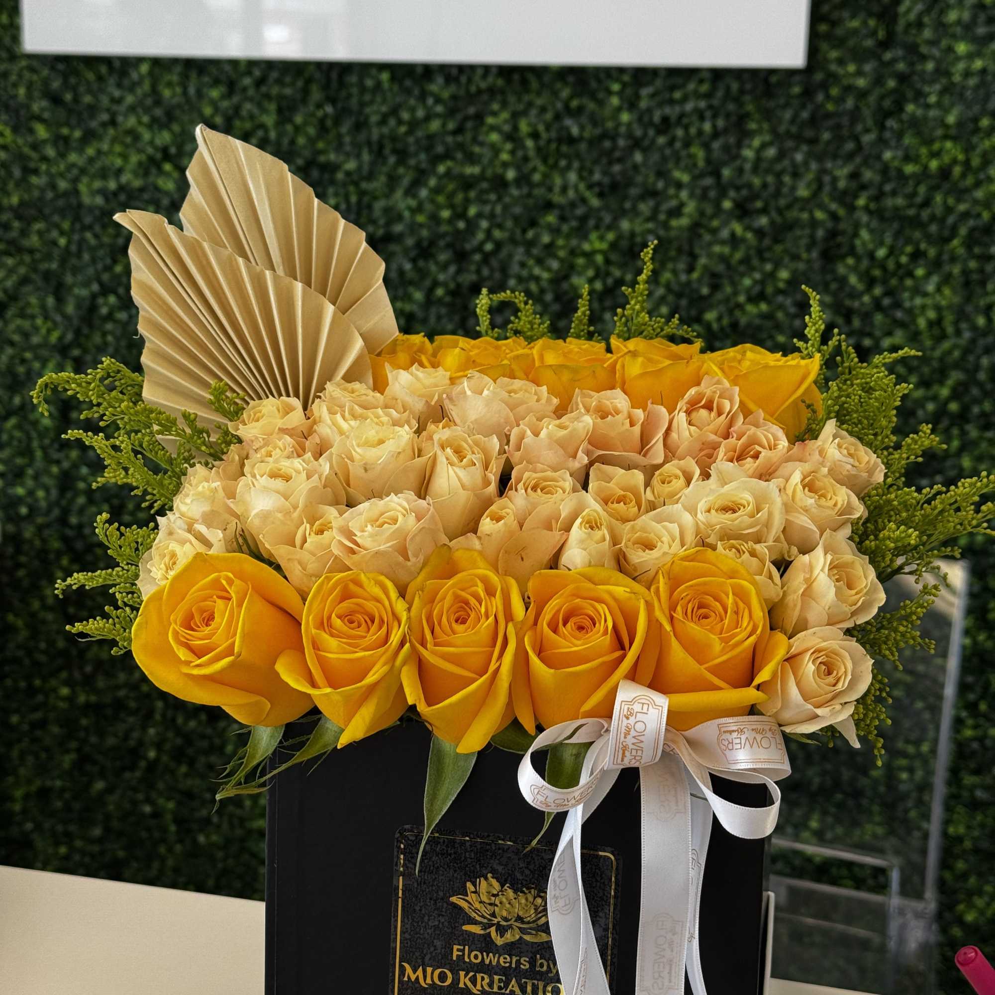 Yellow and cream roses arranged in a black box with a ribbon