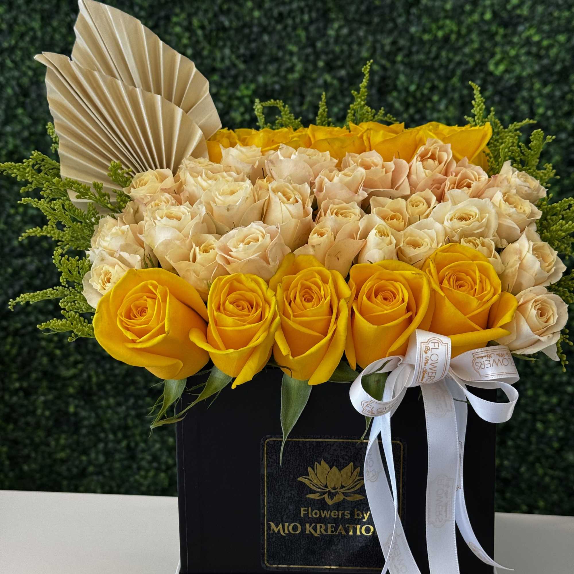 Yellow and cream roses arranged in a black box with ribbon