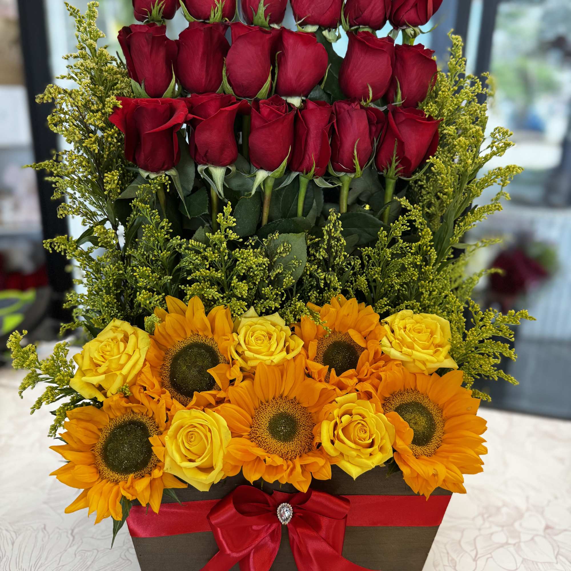 Tiered floral arrangement with red roses, yellow roses, and sunflowers in a box
