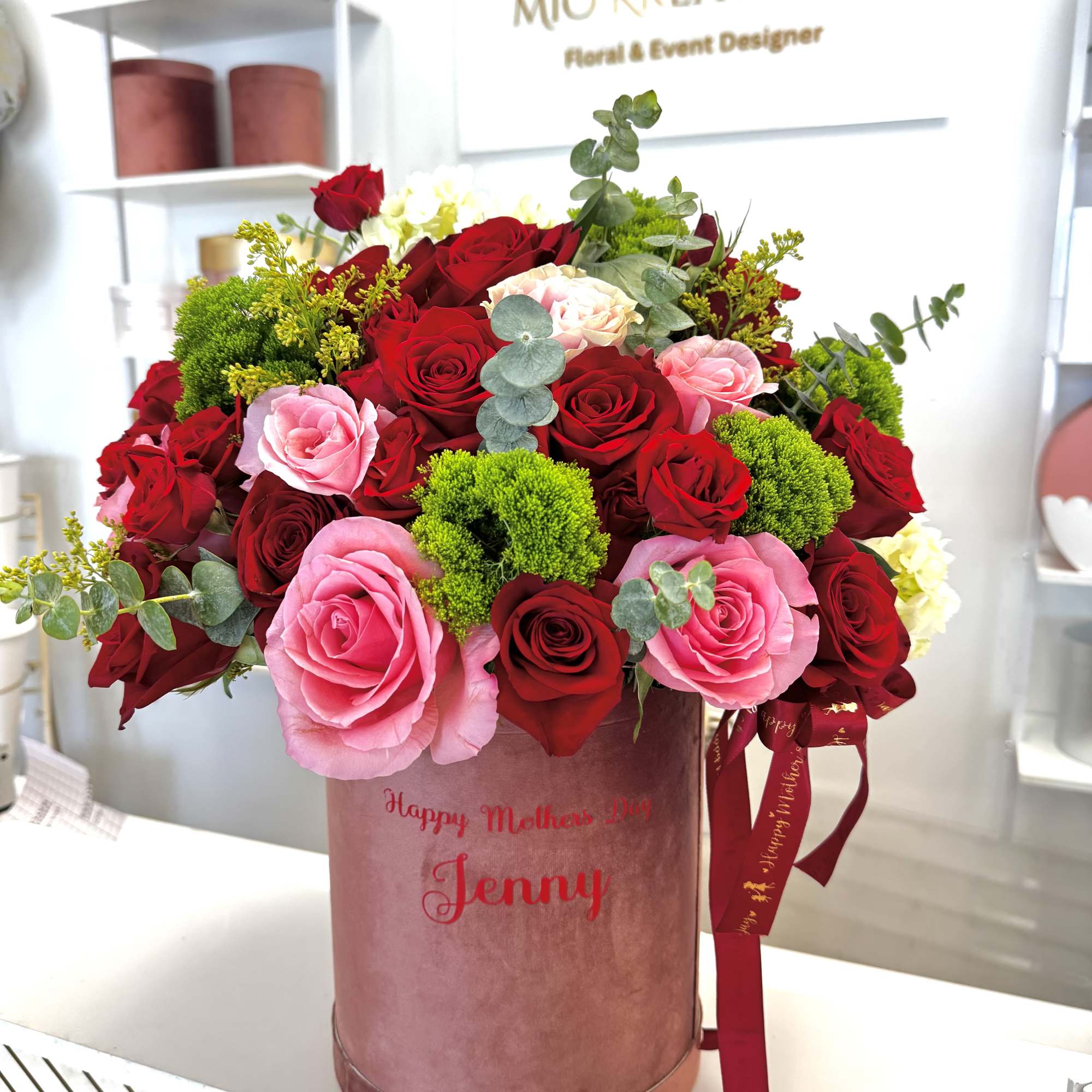 Pink and red roses arranged in a velvet hatbox with ribbon