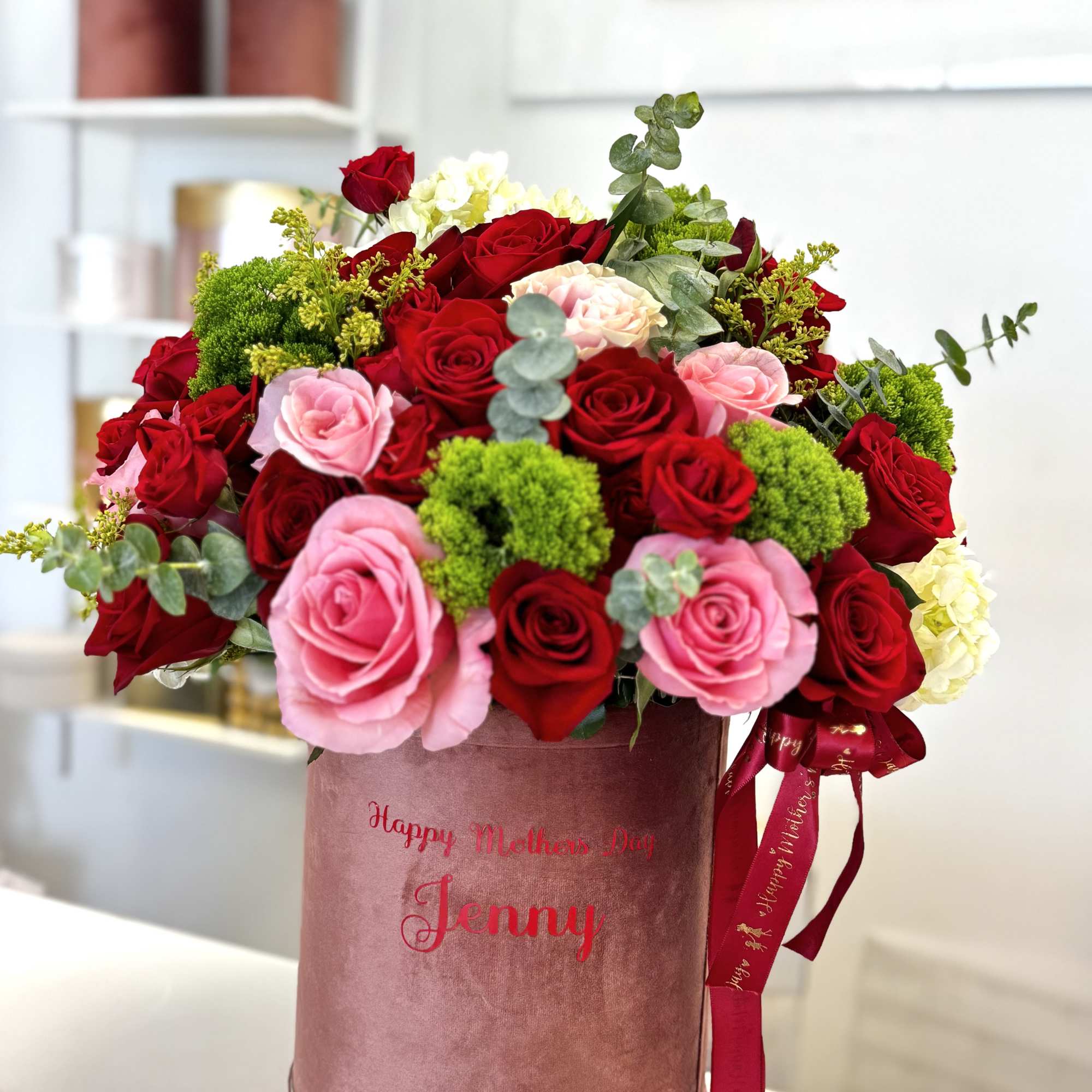 Red and pink roses arranged in a pink hatbox with ribbon