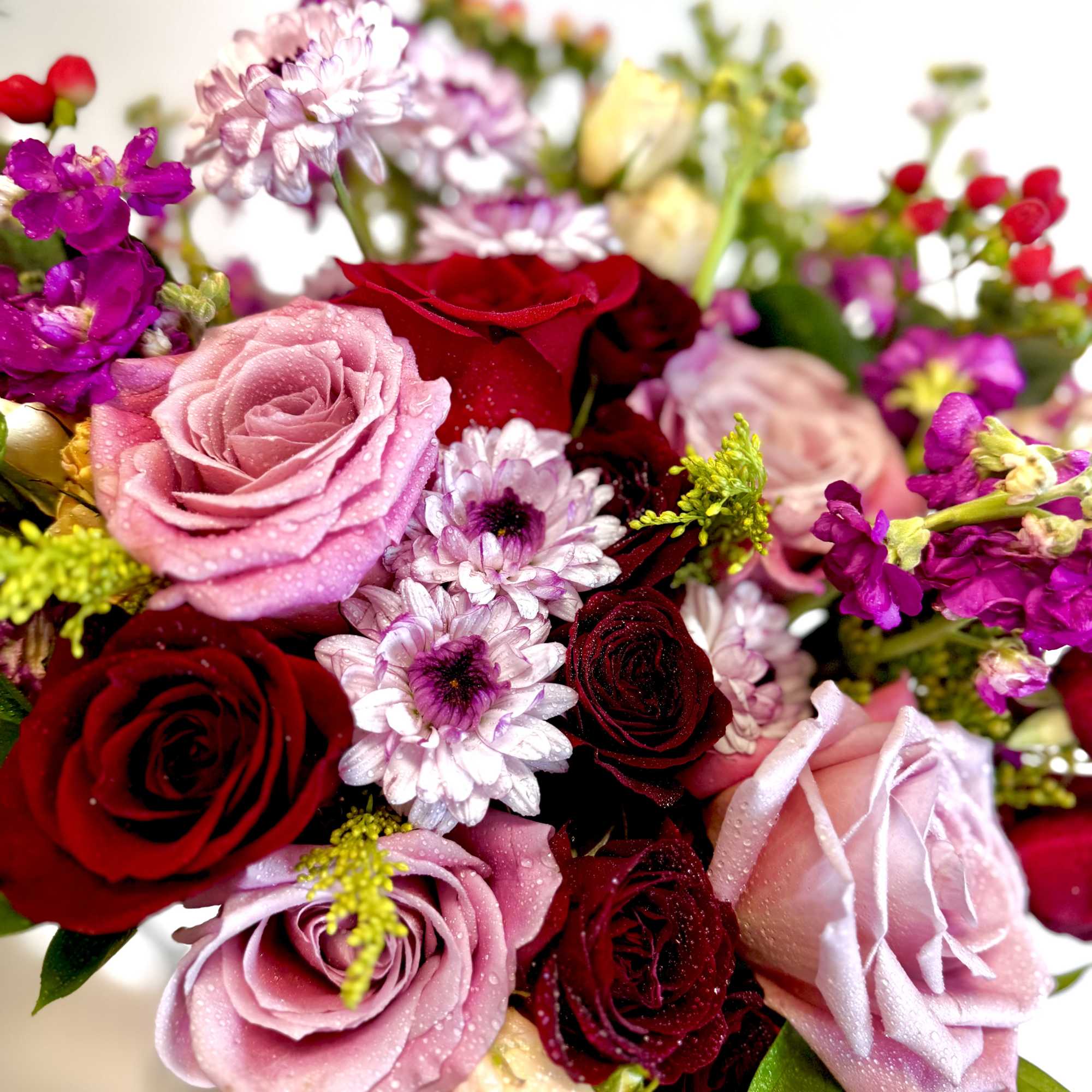 Bouquet of red, pink, and white roses with small purple flowers