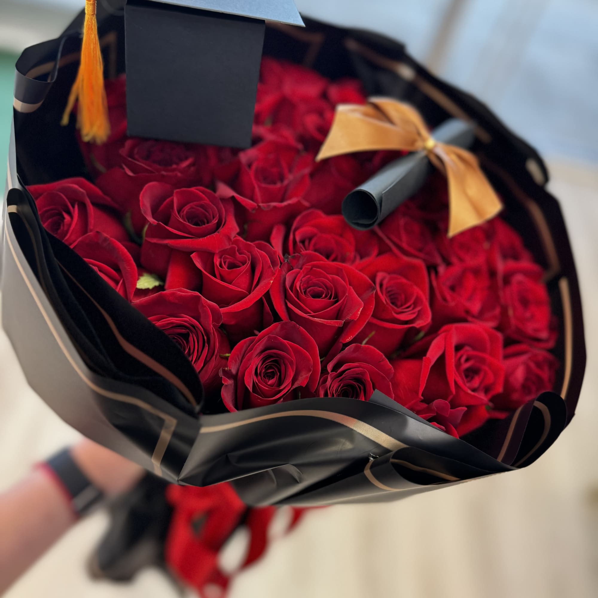 Bouquet of red roses wrapped in black paper with a graduation cap