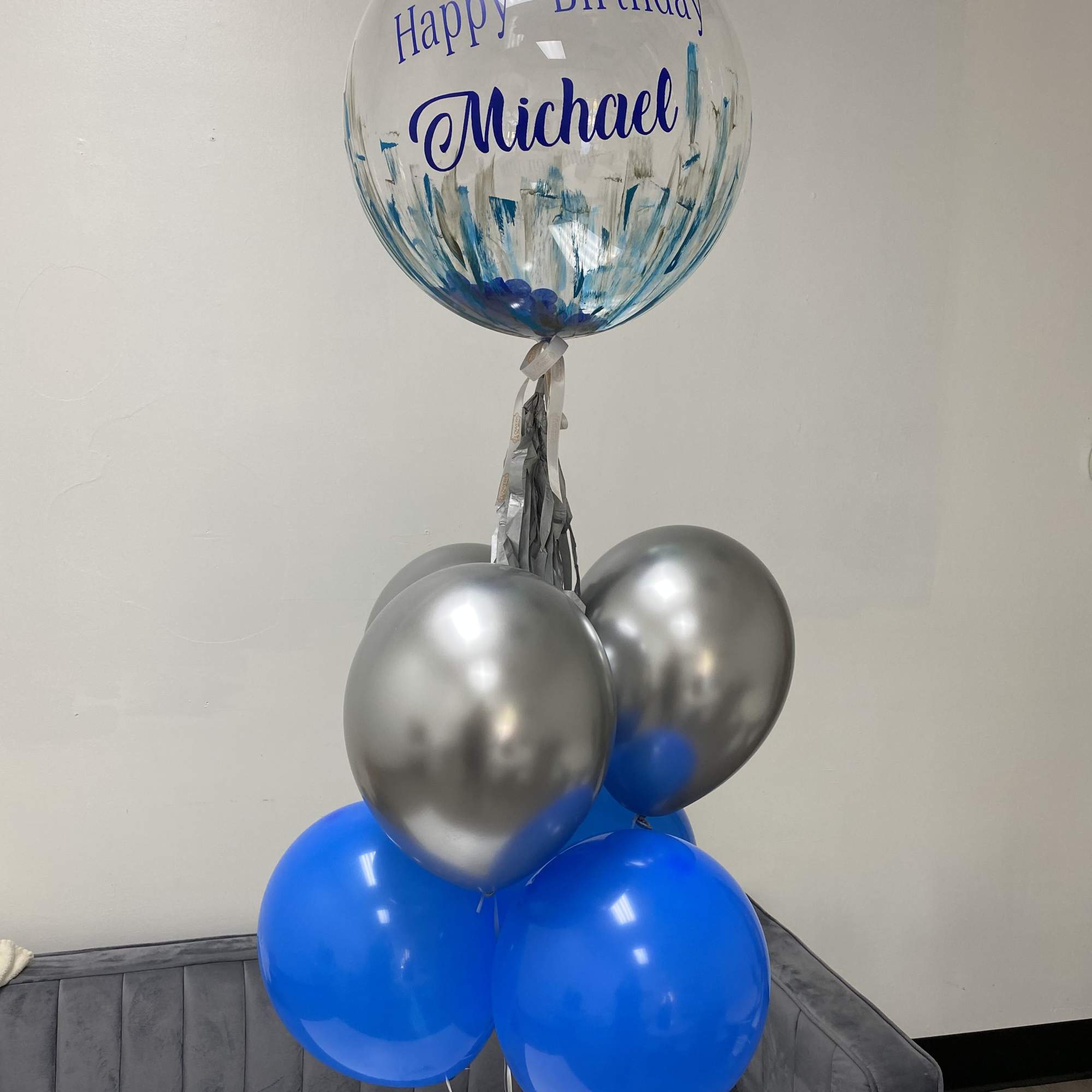 Birthday balloon bouquet with a clear personalized balloon and blue and silver balloons