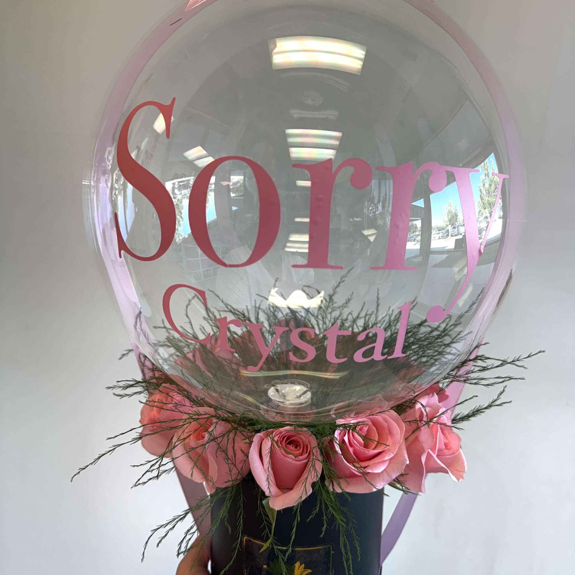 Pink roses arranged around a clear balloon with a pink bow