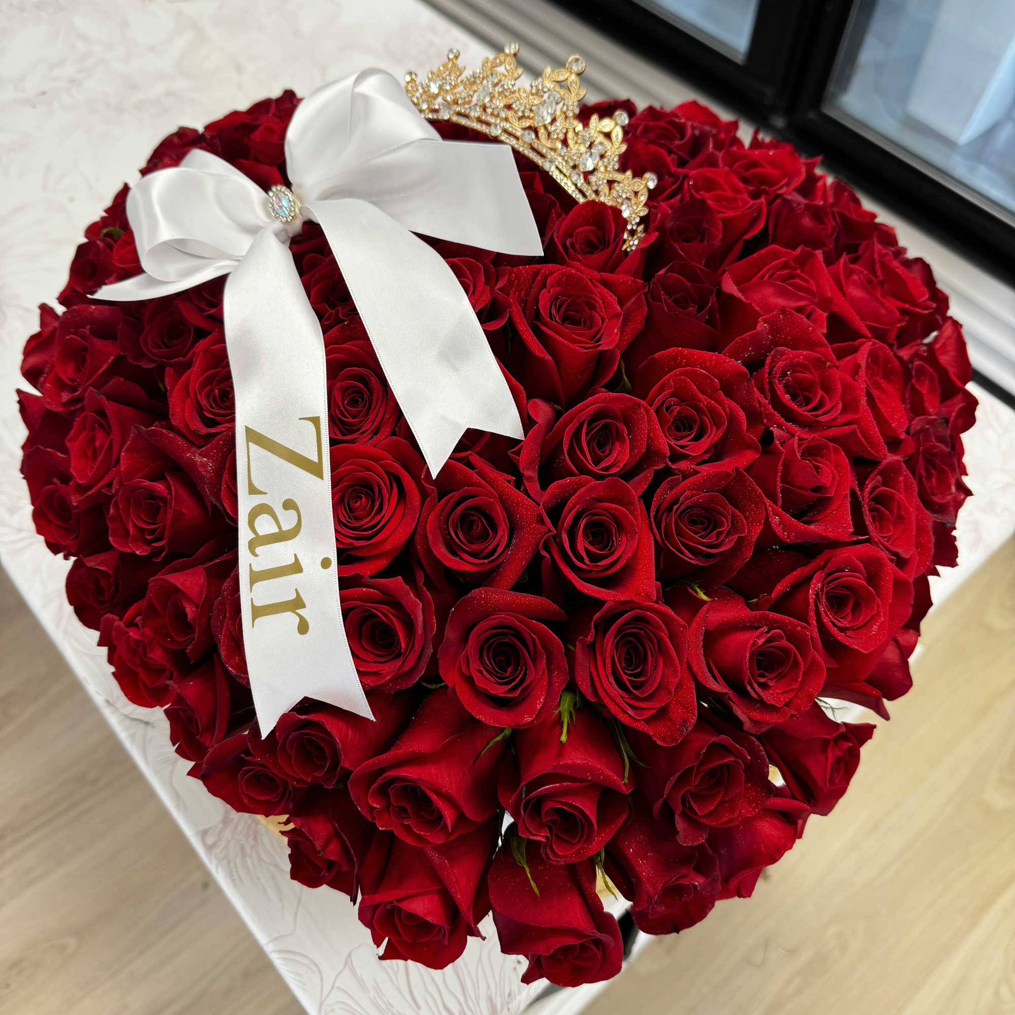 Heart-shaped bouquet of red roses with a white ribbon and gold crown