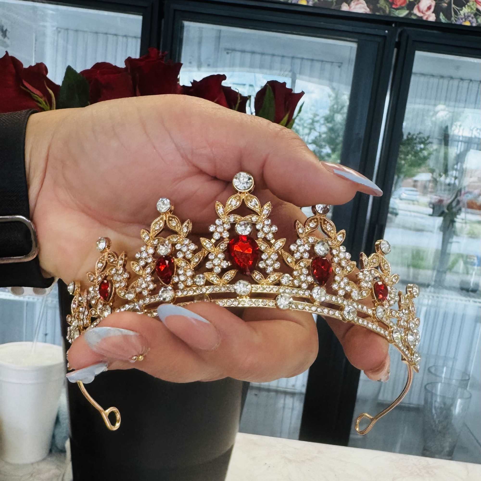 Hand holding a jeweled tiara in front of red roses
