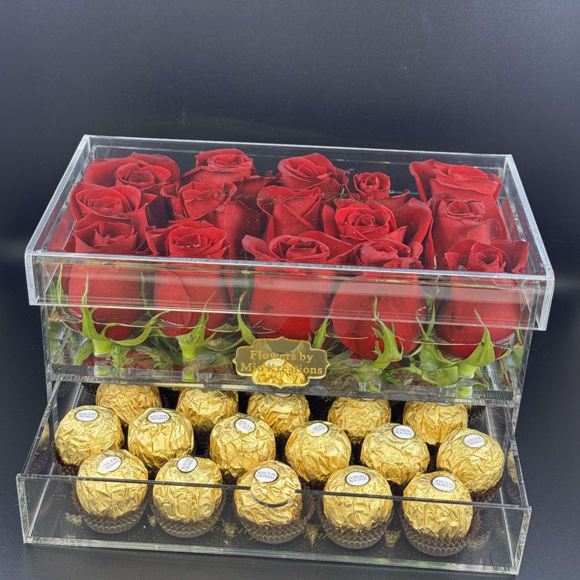 Red roses in a clear acrylic box above gold-wrapped chocolates
