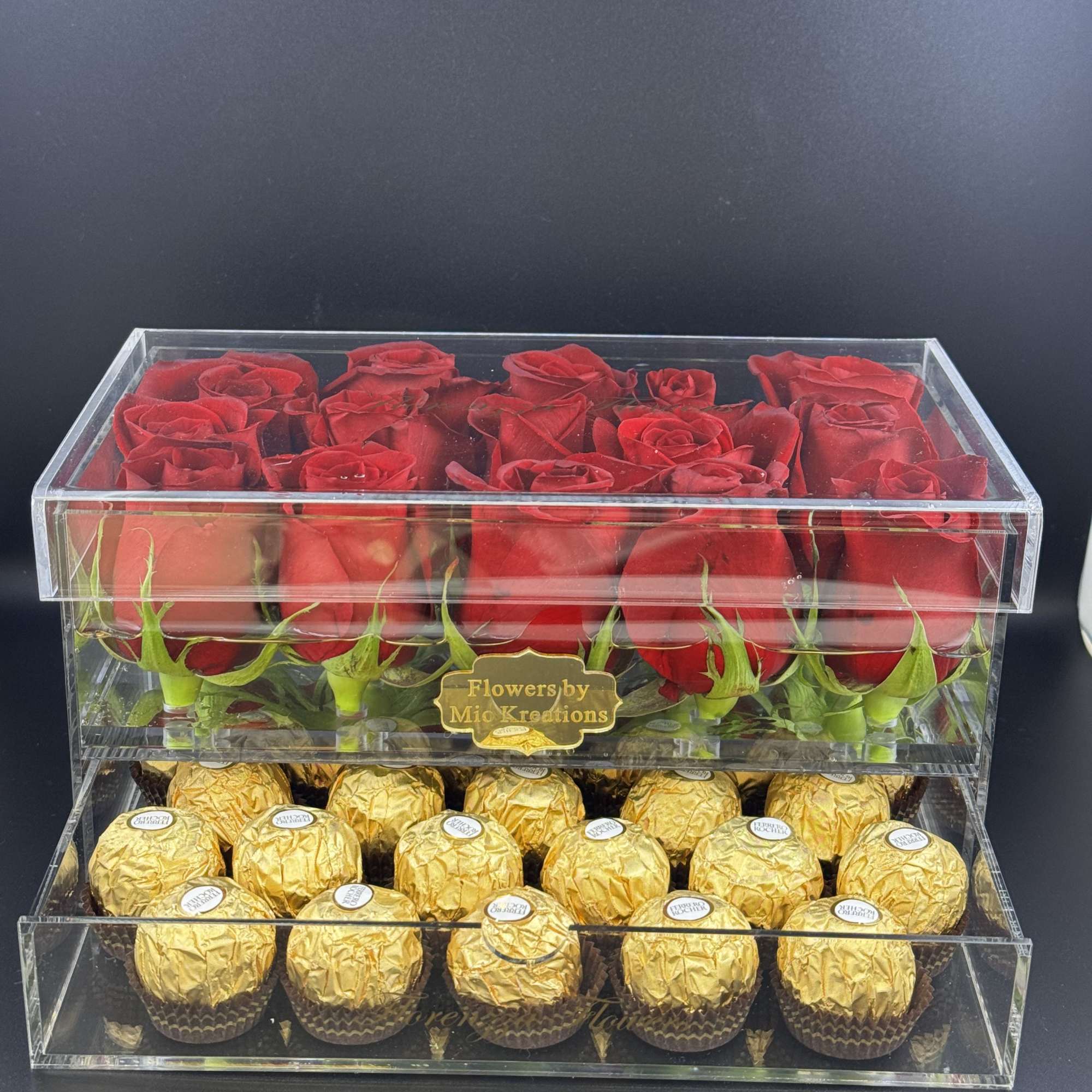 Clear gift box with red roses on top and gold-wrapped chocolates below