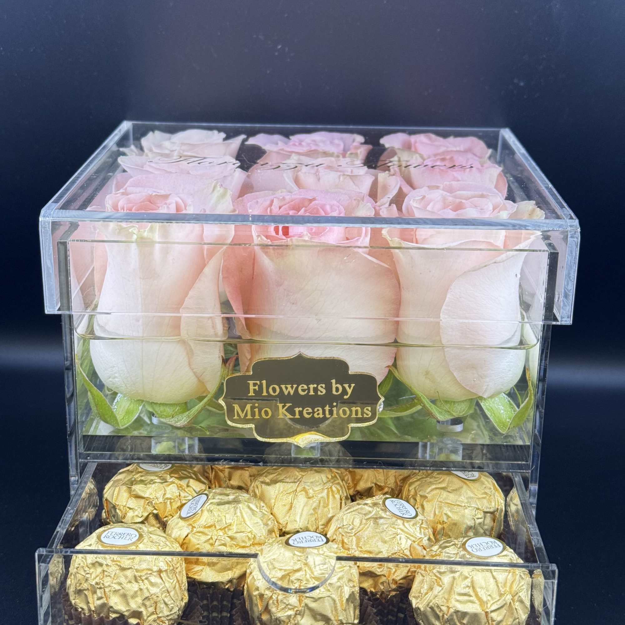 Pink roses in a clear box above gold-wrapped chocolates