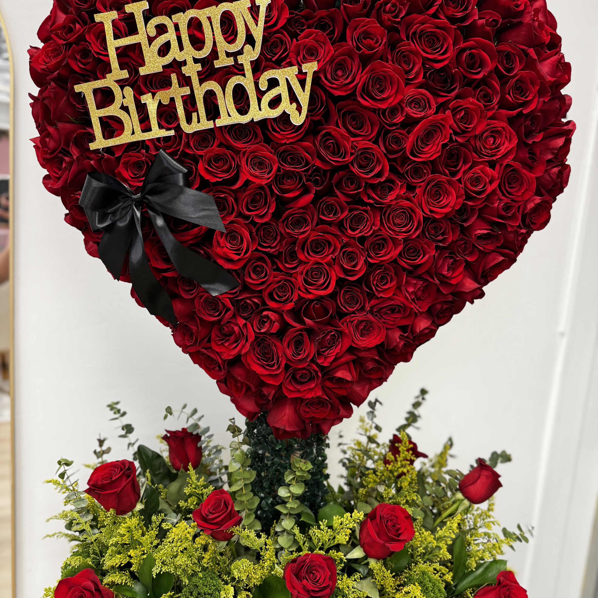 Heart-shaped red rose arrangement with a gold Happy Birthday sign and black bow