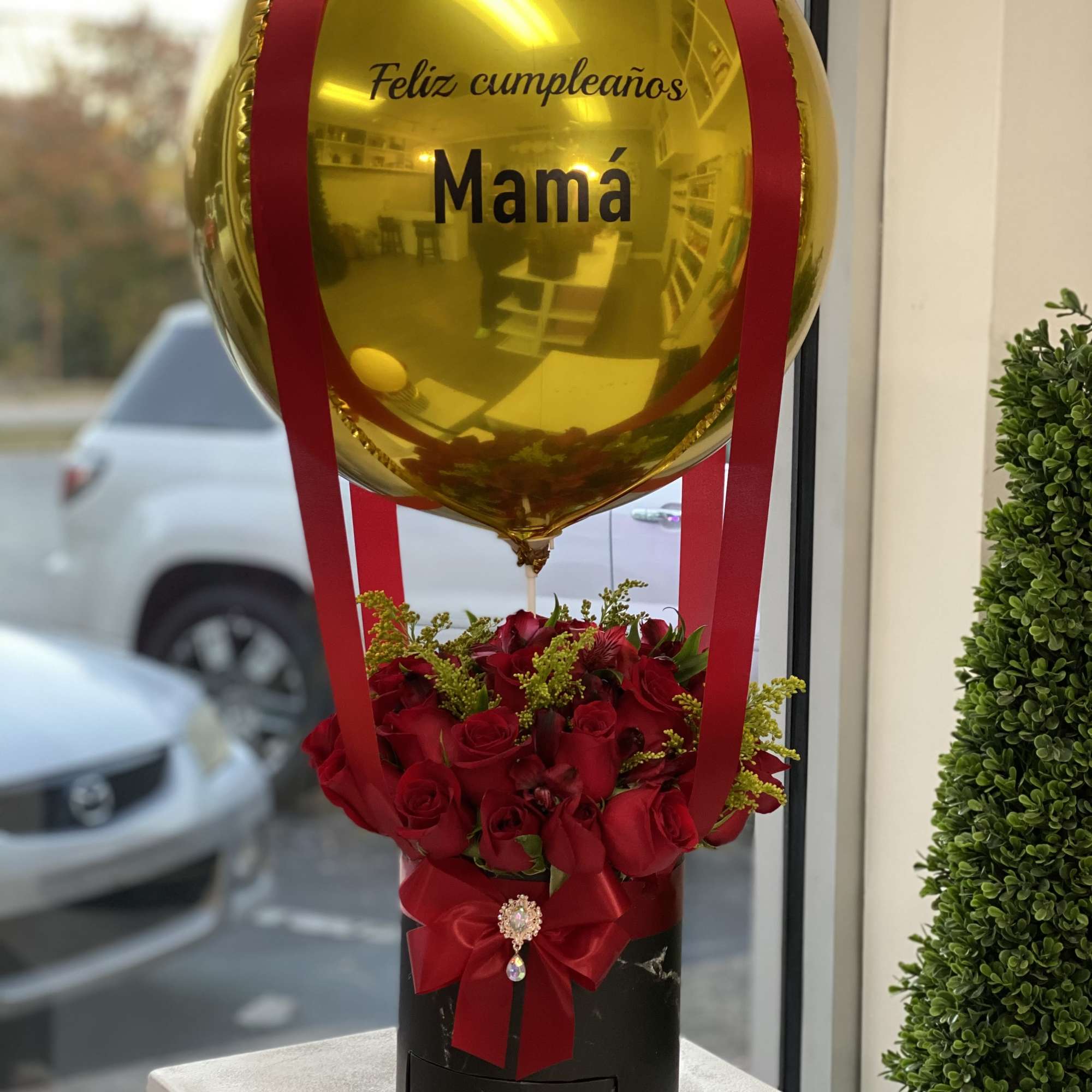 Gold balloon above red roses in a black box with a red bow