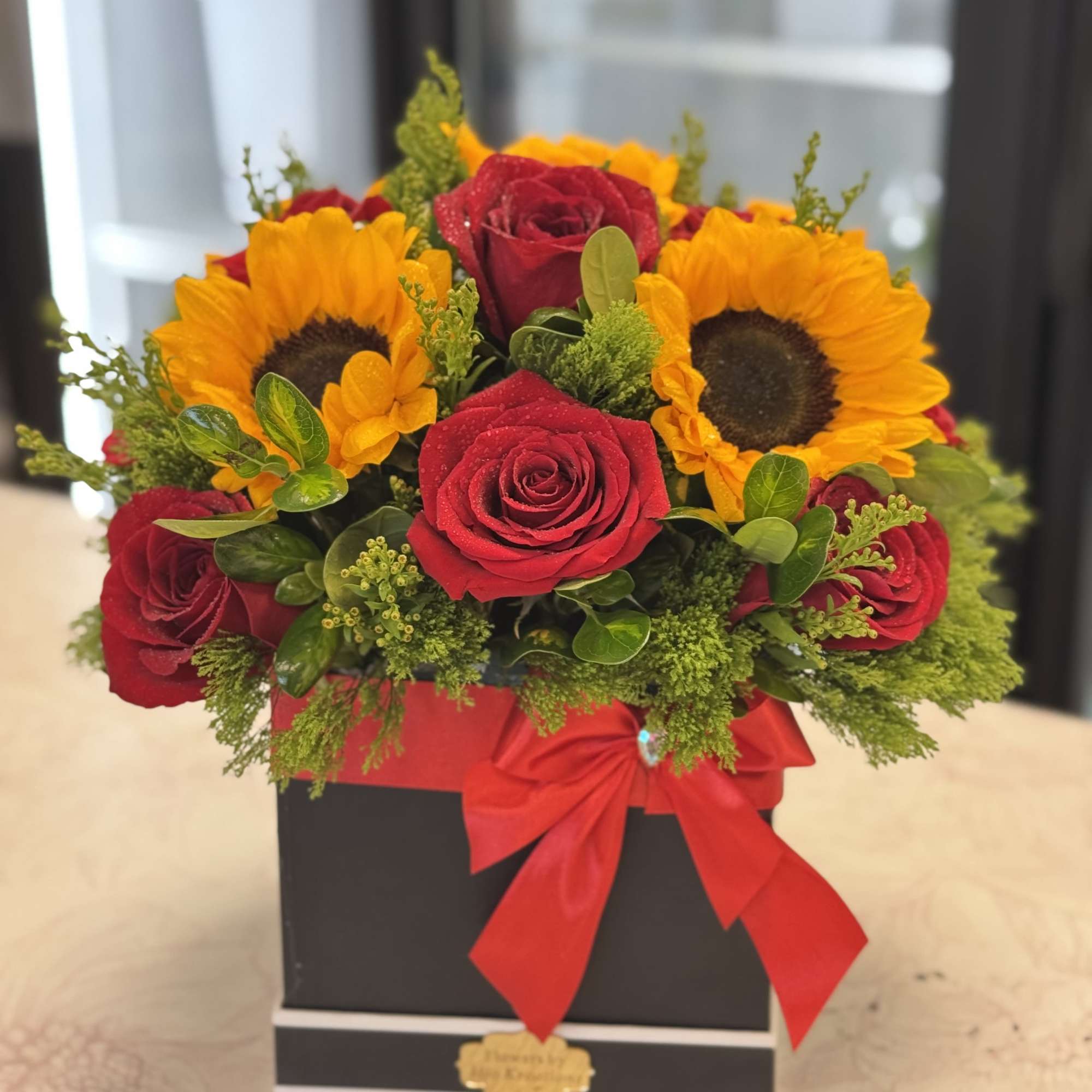 Red roses and sunflowers in a black box with a red ribbon