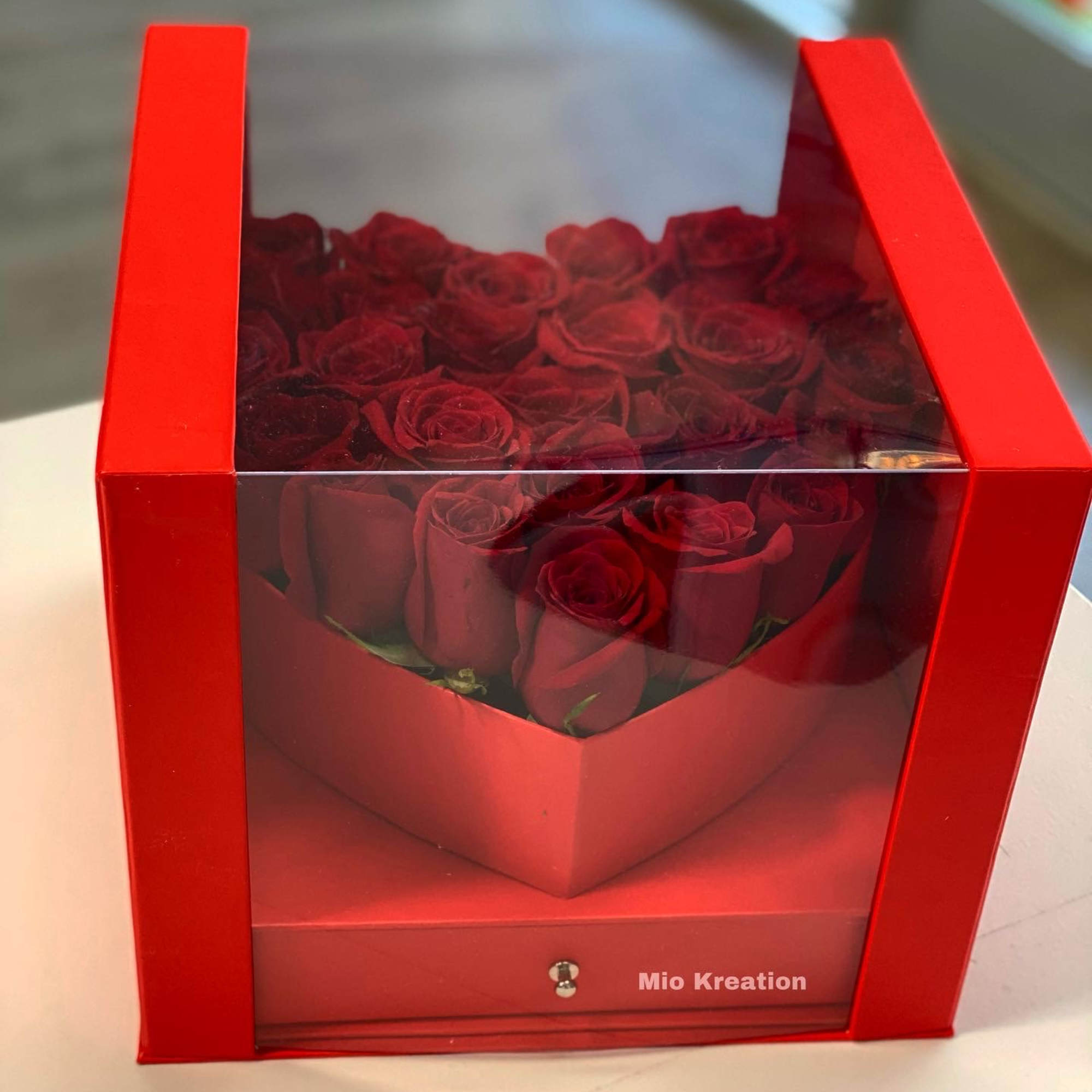 Red roses arranged in a red gift box with a clear lid