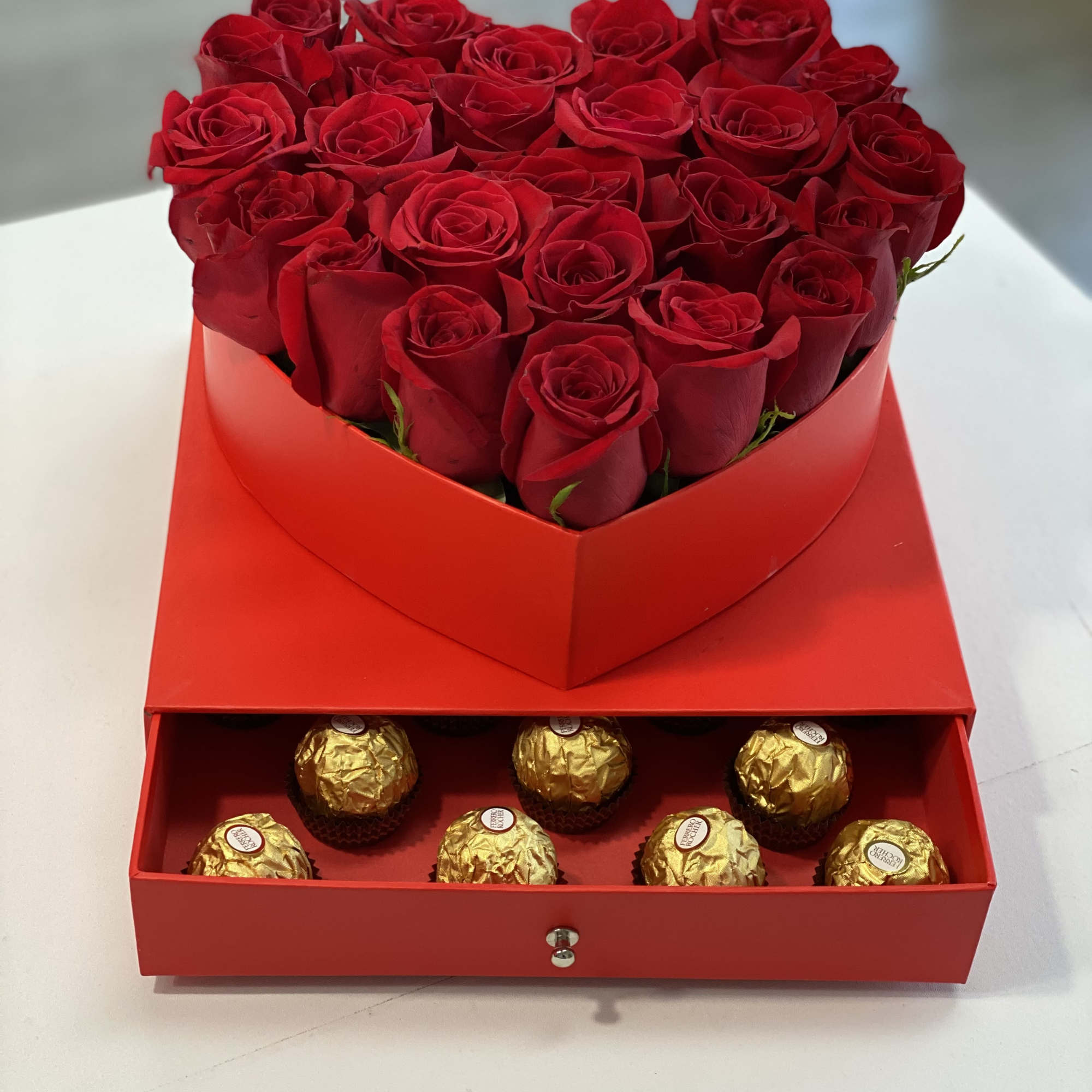 Red roses in a heart-shaped box above gold-wrapped chocolates in a drawer