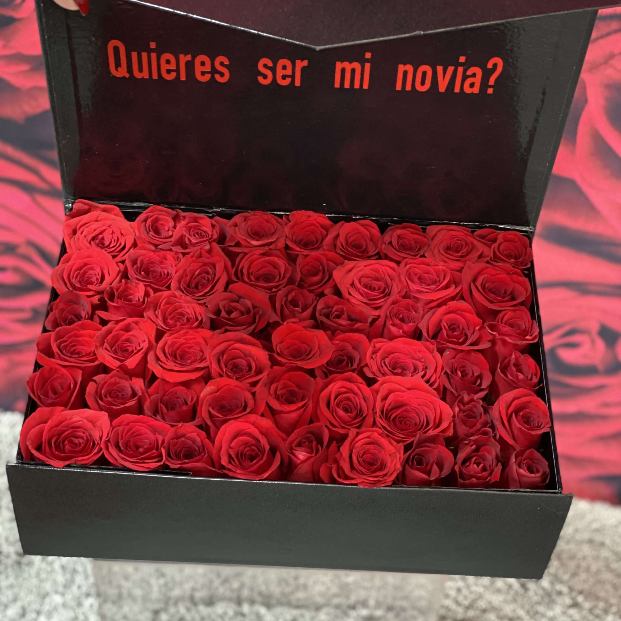 Black gift box filled with red roses and Spanish text on the lid
