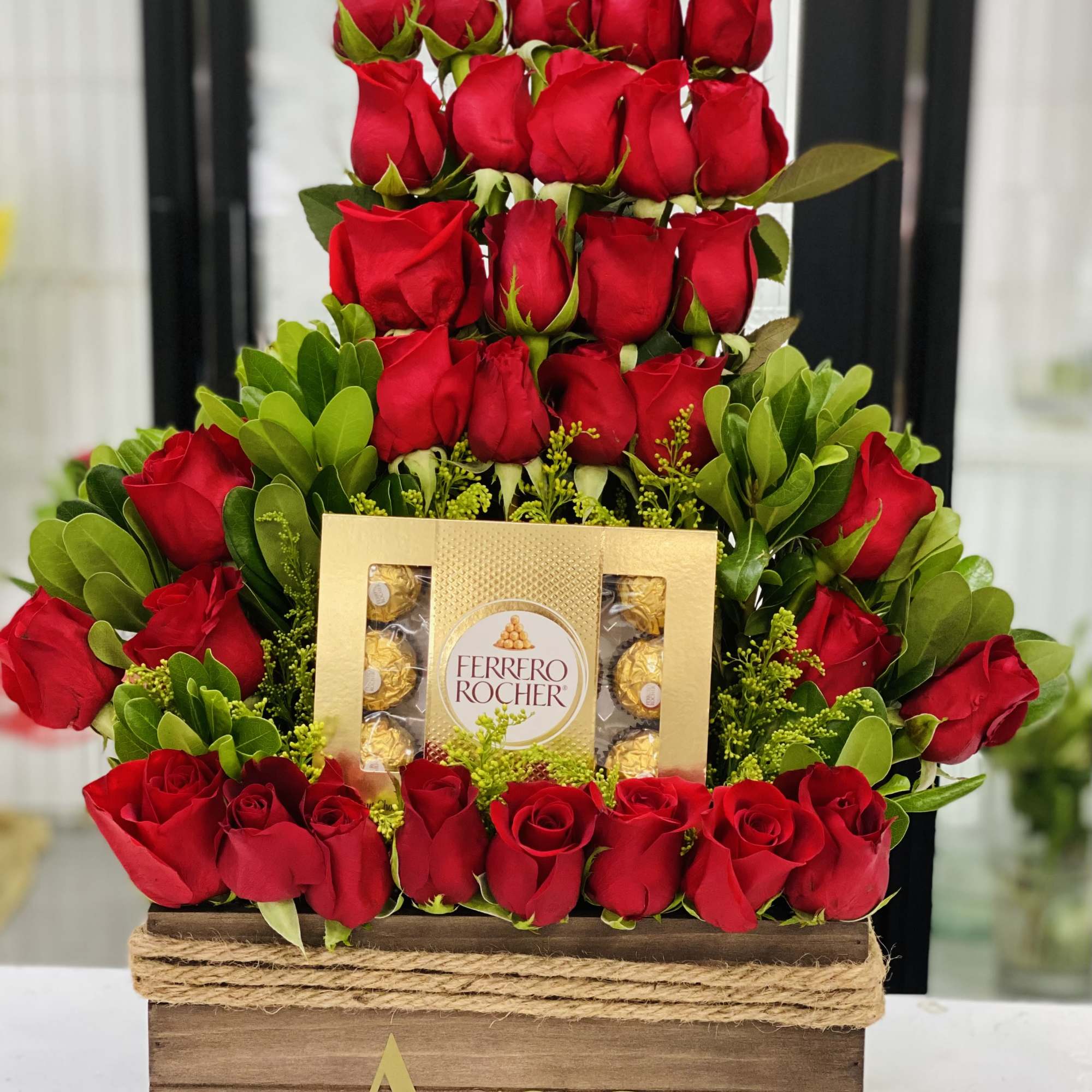 Tiered red rose arrangement with a Ferrero Rocher box in a wooden crate