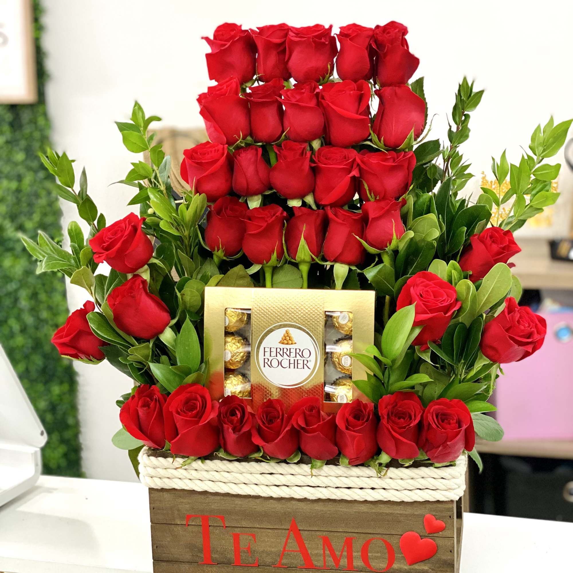Red roses arranged around a Ferrero Rocher box in a wooden gift crate