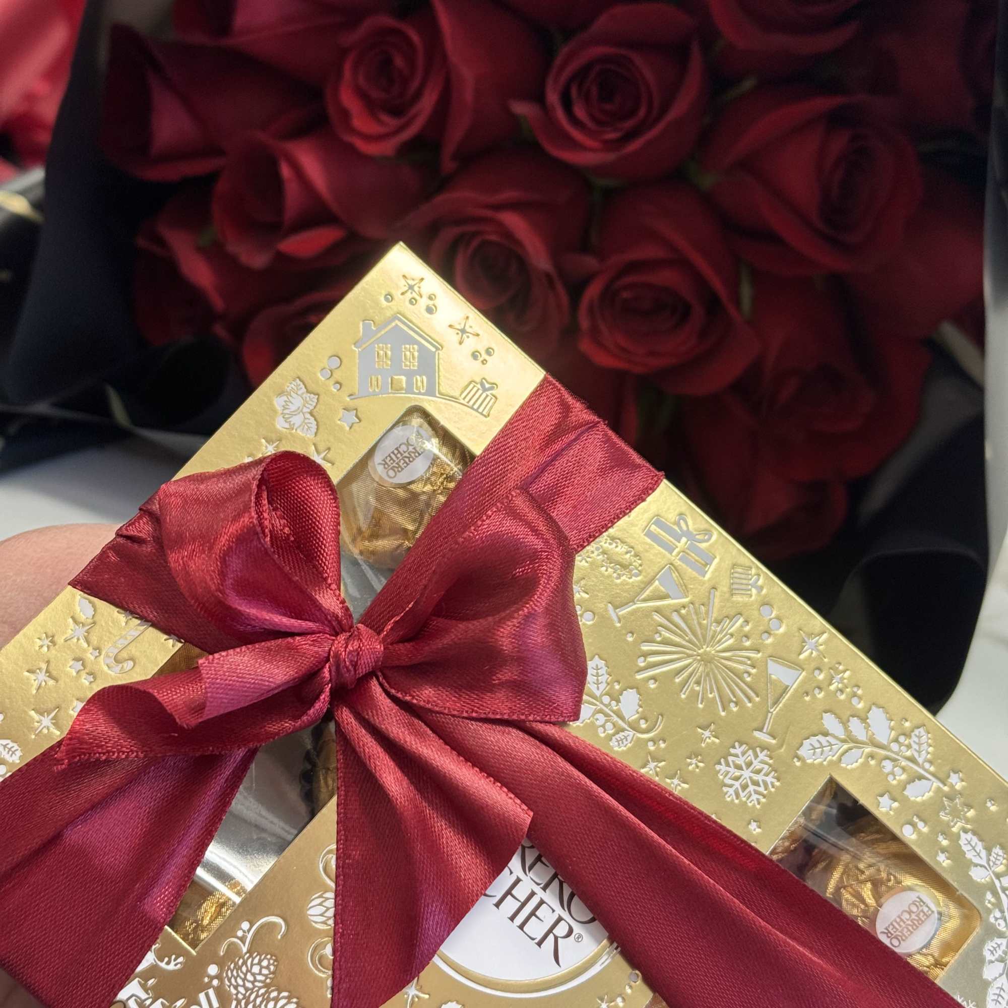Red roses with a gold chocolate gift box tied in a red ribbon