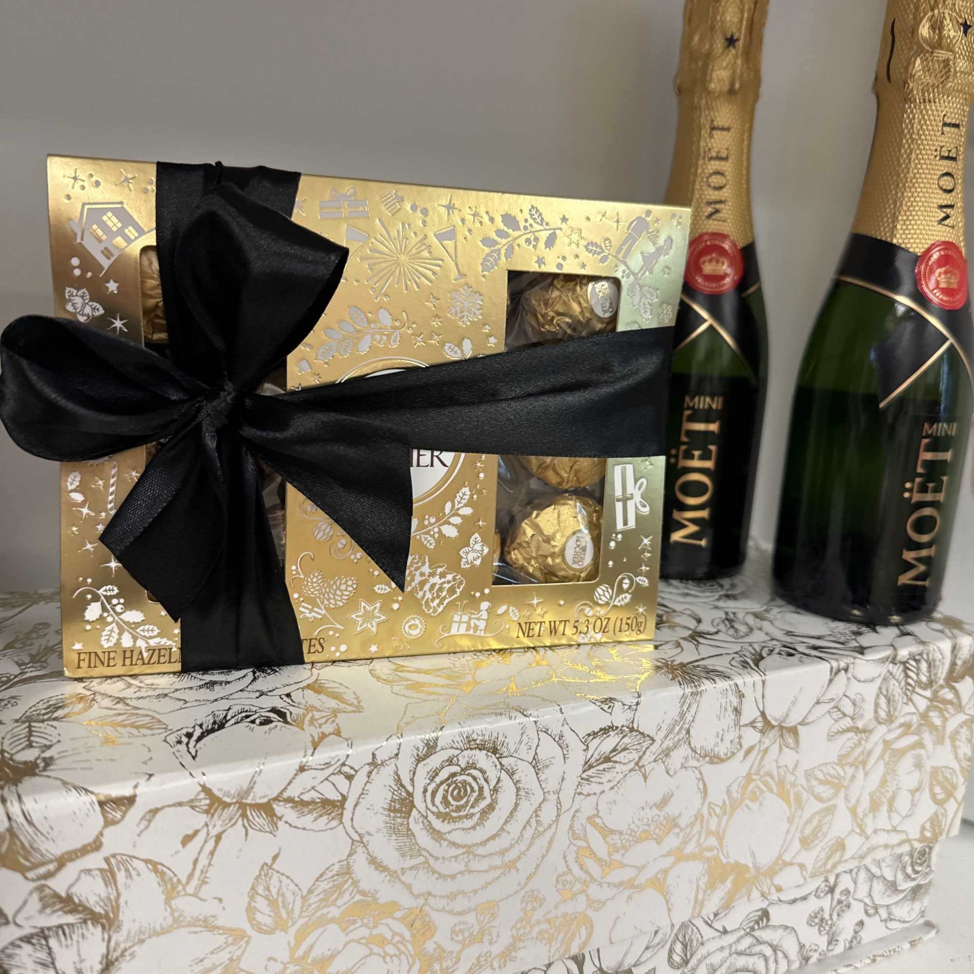 Gift box with chocolates and two mini Moet bottles tied with a black ribbon