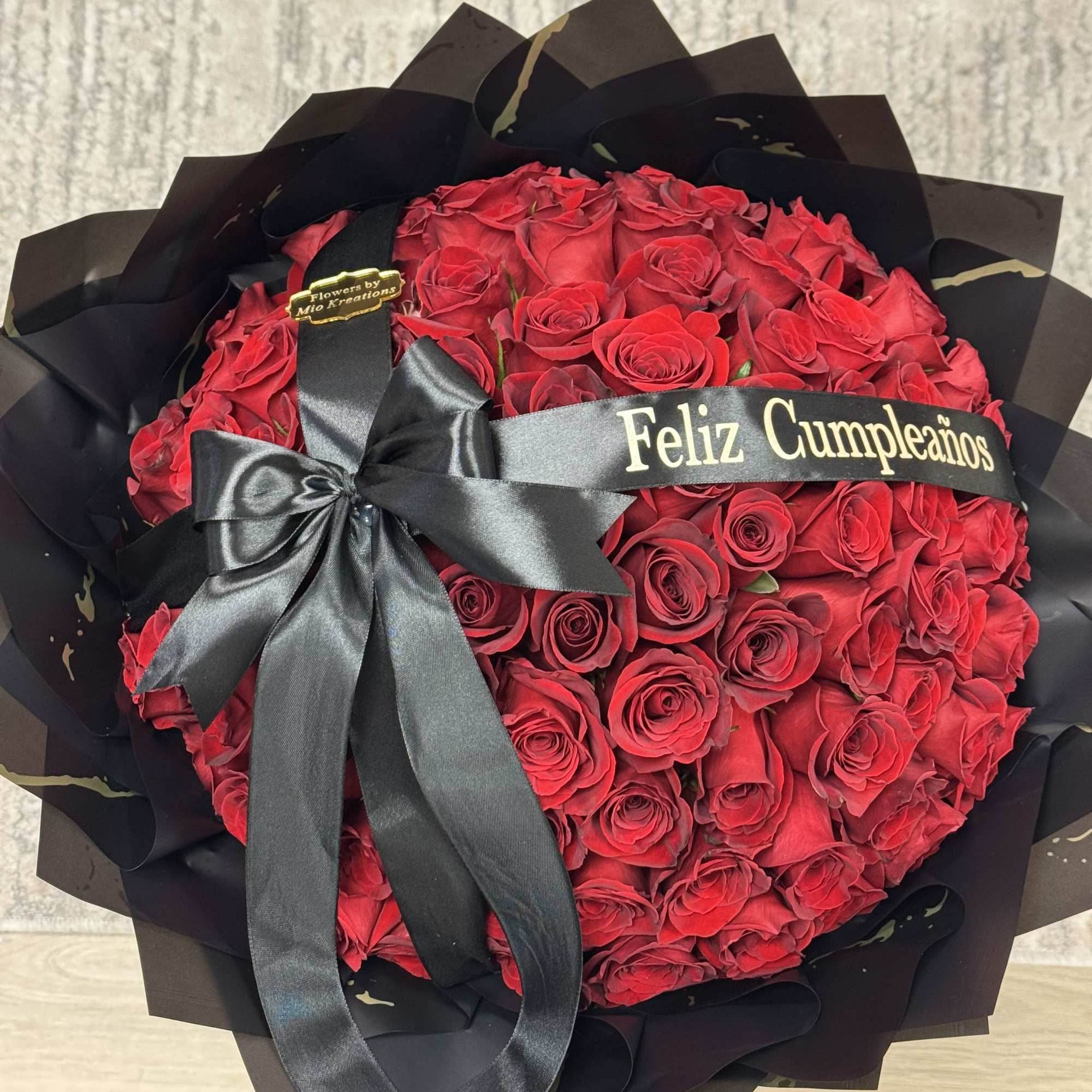 Round bouquet of red roses wrapped in black paper with a black ribbon